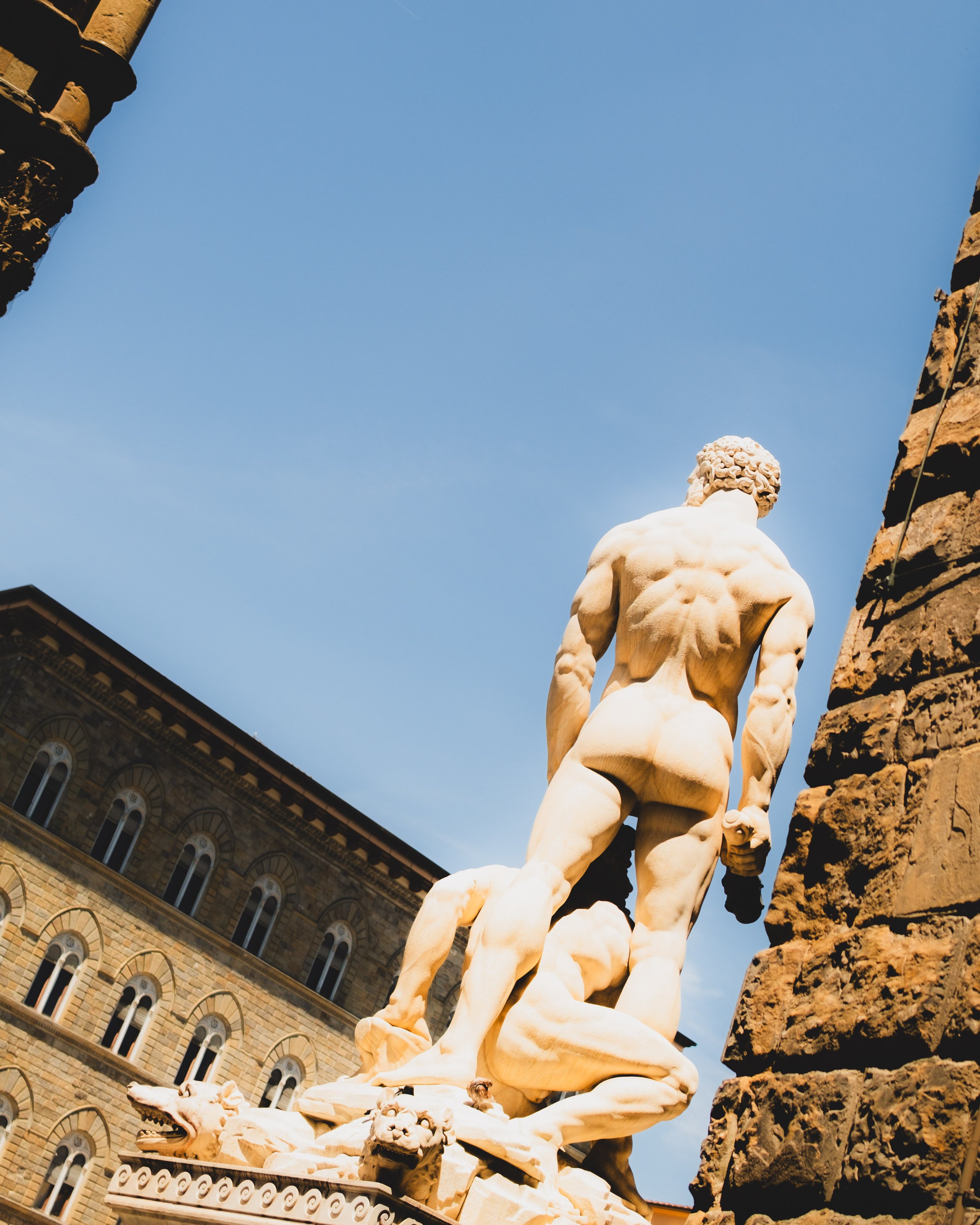 Marble statue of a muscular male figure seen from behind, outdoors with a historic building in the background. Lionel Chu - Hotel & Travel Photographer