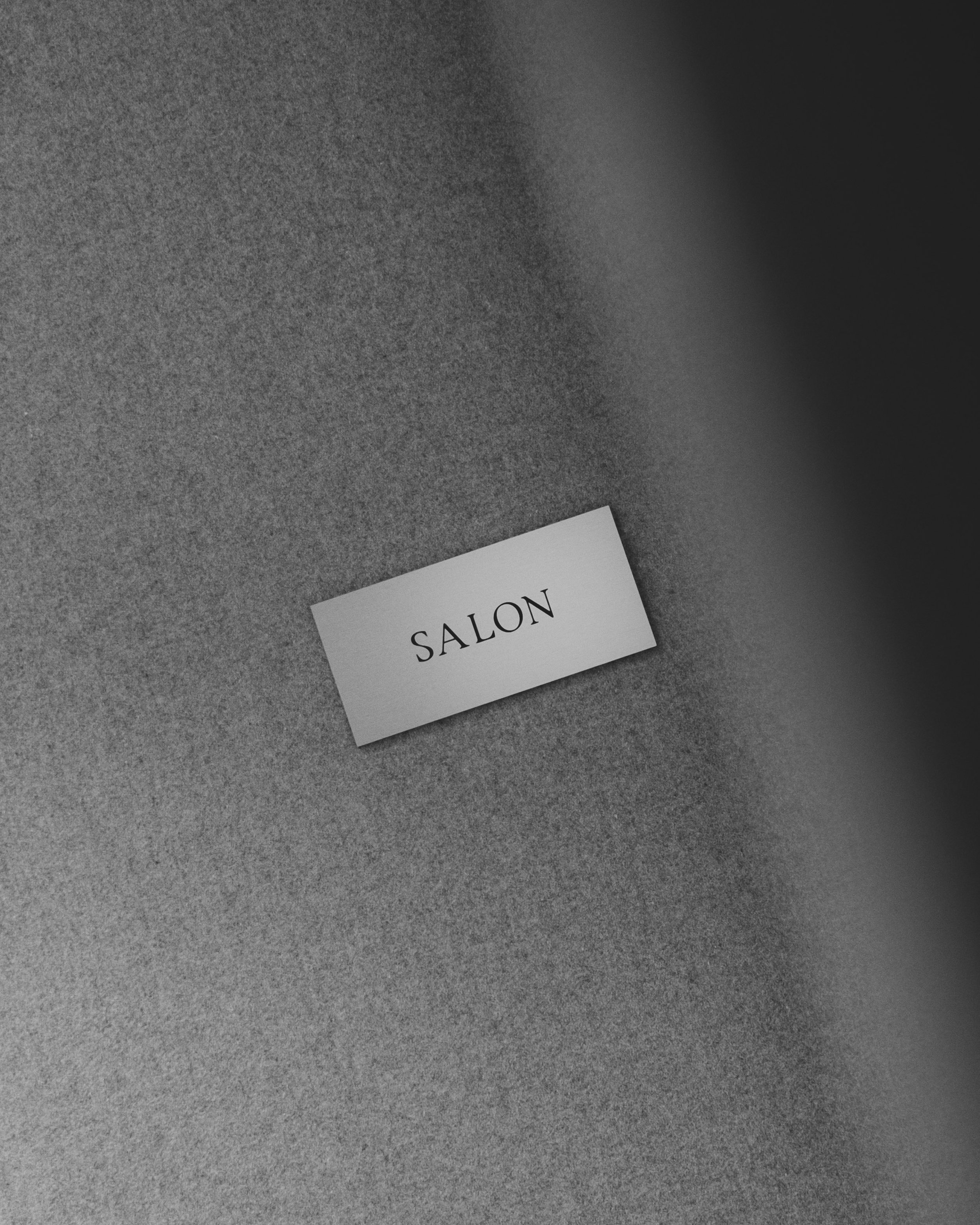 A small white card with the word 'SALON' printed in black capital letters on a gray surface.