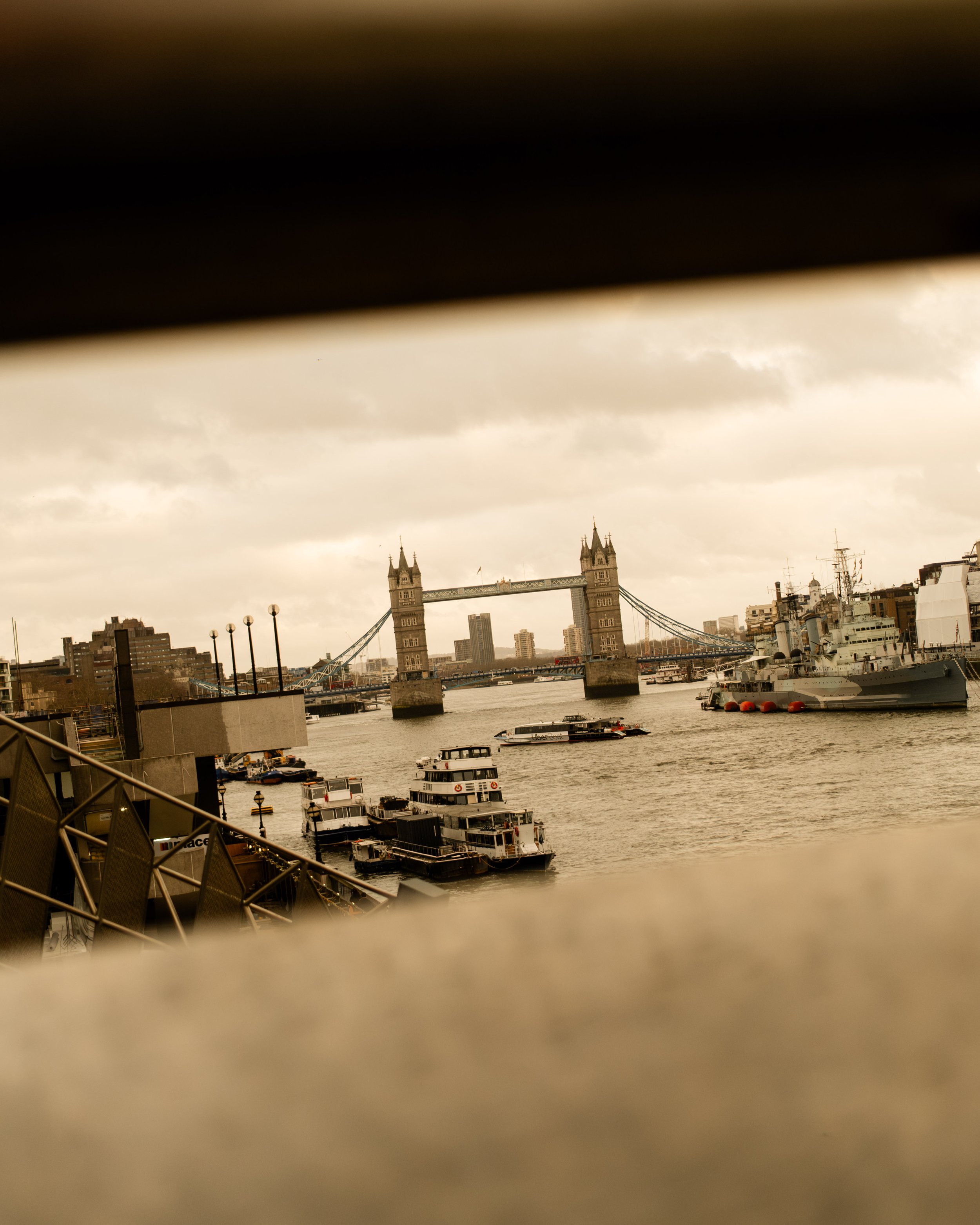 View of Tower Bridge in London with boats on the River Thames, seen through a partially obscured window. Lionel Chu - Hotel & Travel Photographer