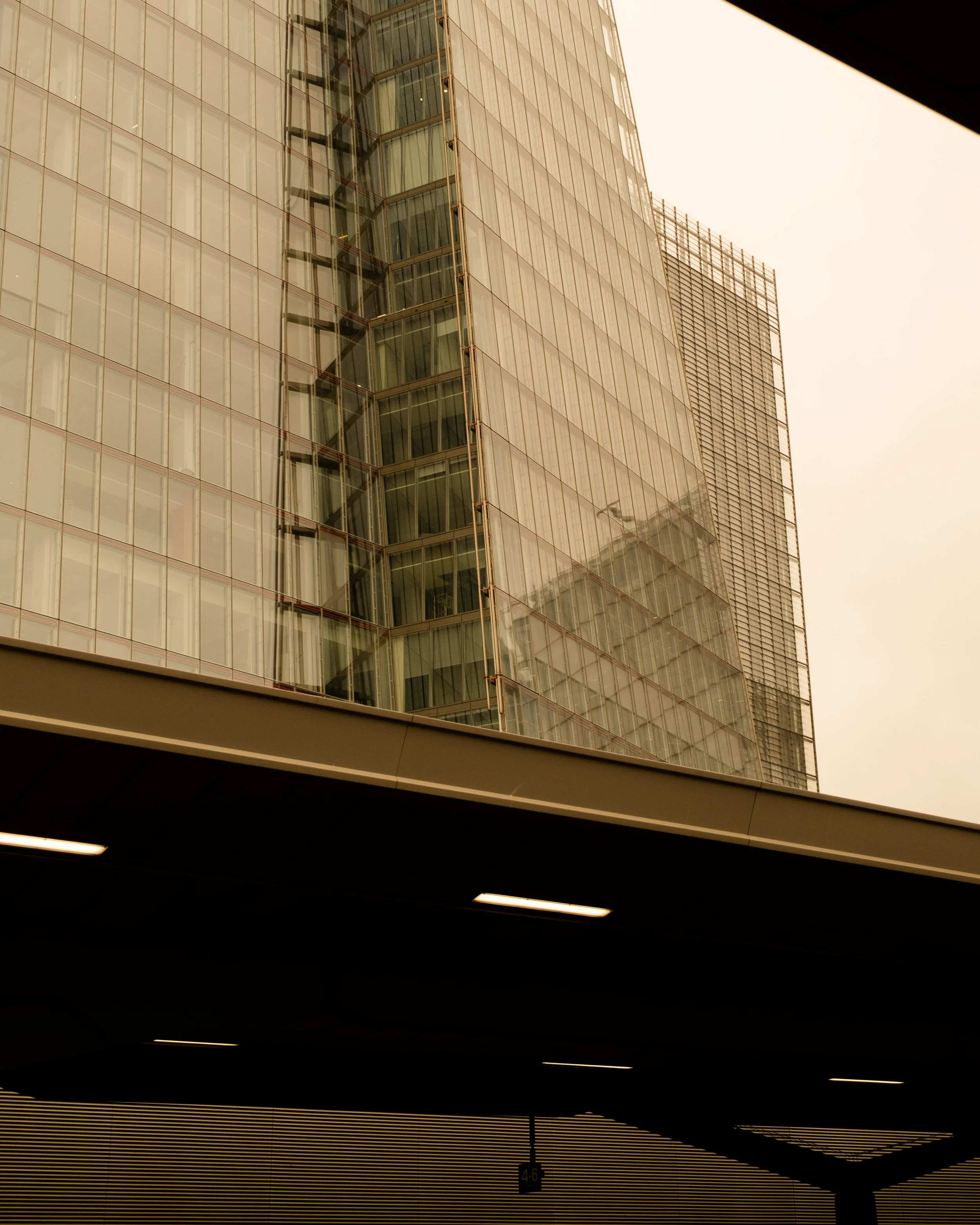 Modern glass high-rise building with reflecting windows, viewed from below in an urban area, with part of a parking structure or street level in the foreground. Lionel Chu - Hotel & Travel Photographer