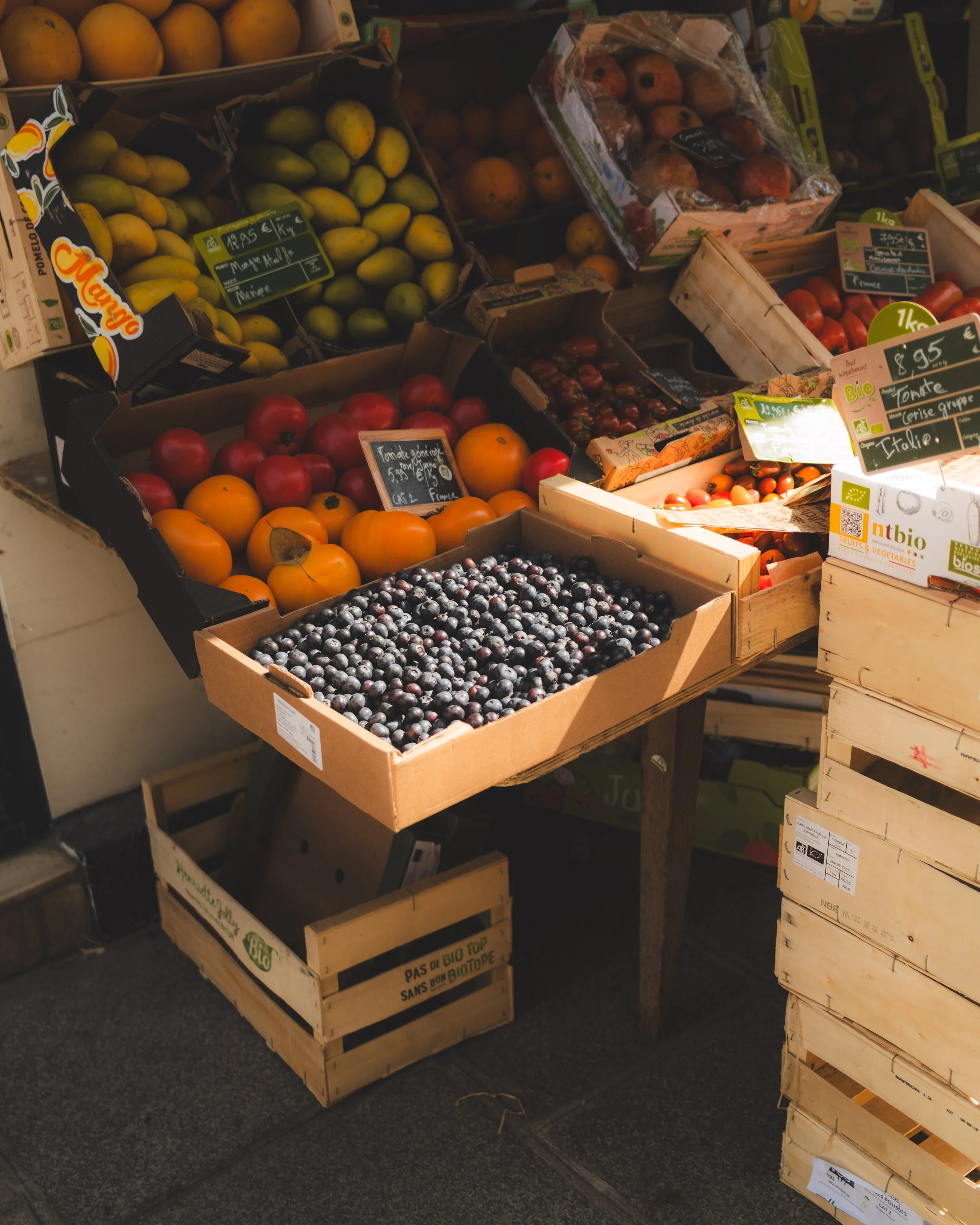 Display of various fruits in wooden and cardboard crates at a grocery store, including yellow and red apples, blueberries, and pomegranates.