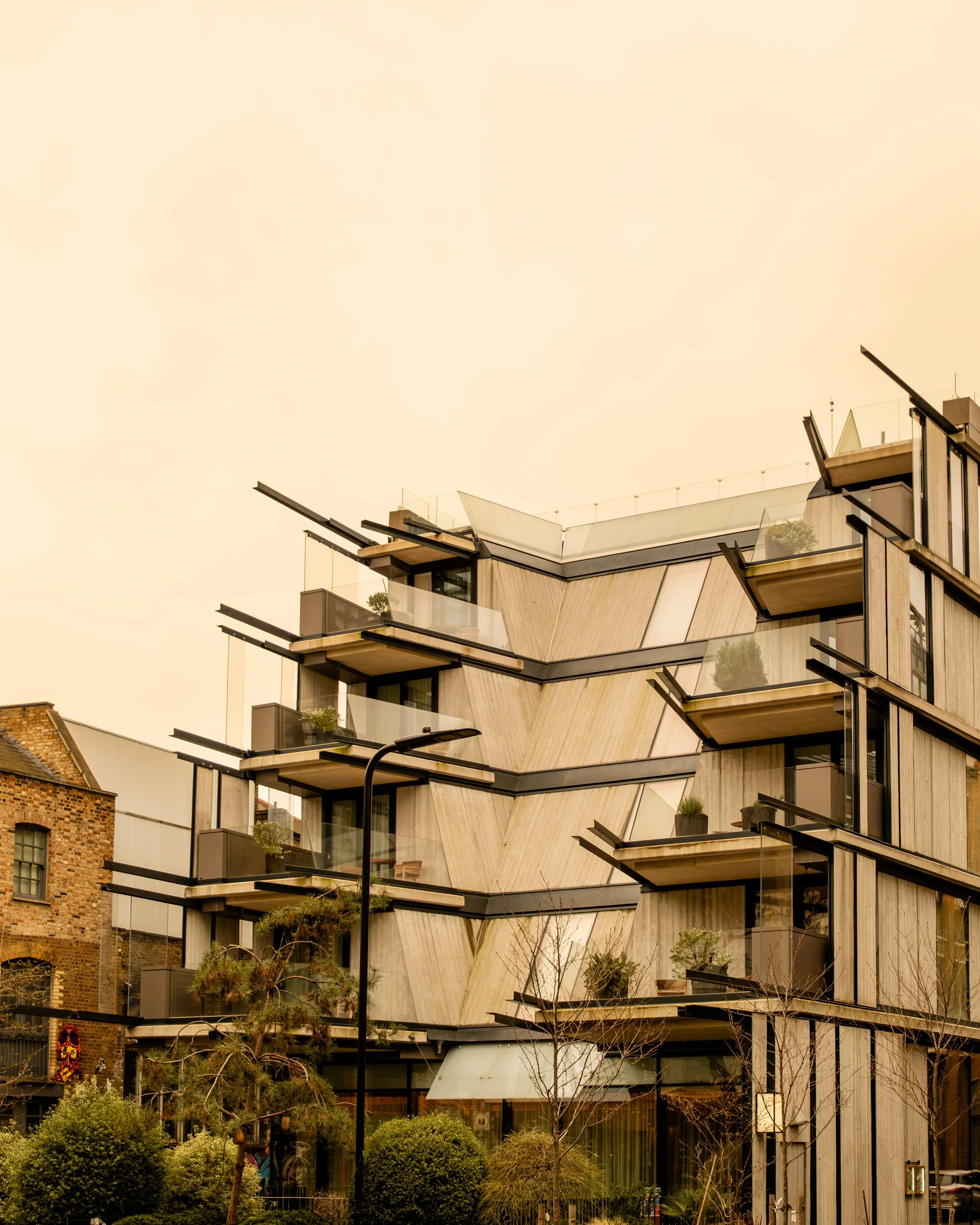 Modern multi-story building with angular design and glass balconies, surrounded by trees and a streetlamp. Lionel Chu - Hotel & Travel Photographer