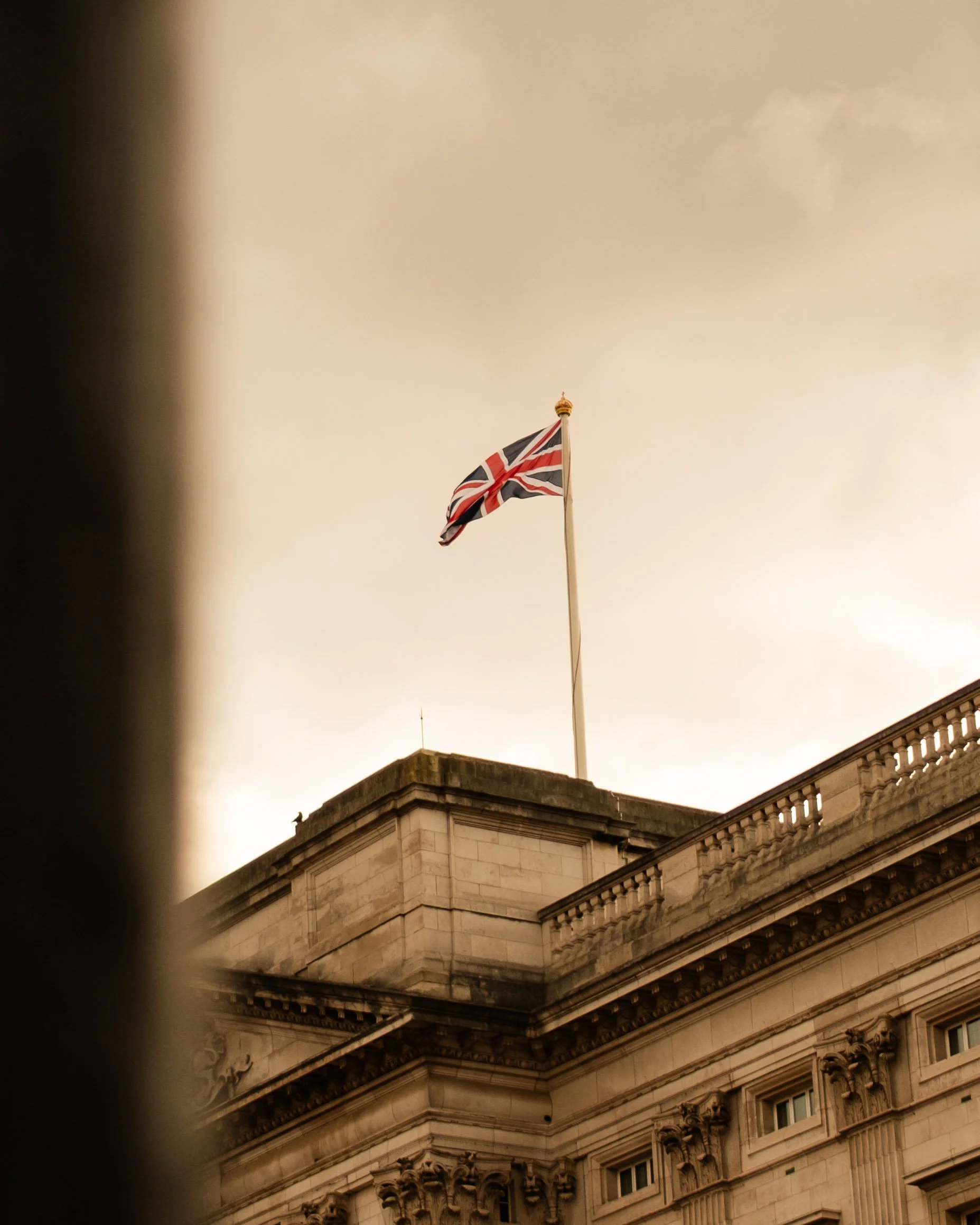 British flag flying atop a historic stone building with ornate architectural details, against a cloudy sky. Lionel Chu - Hotel & Travel Photographer