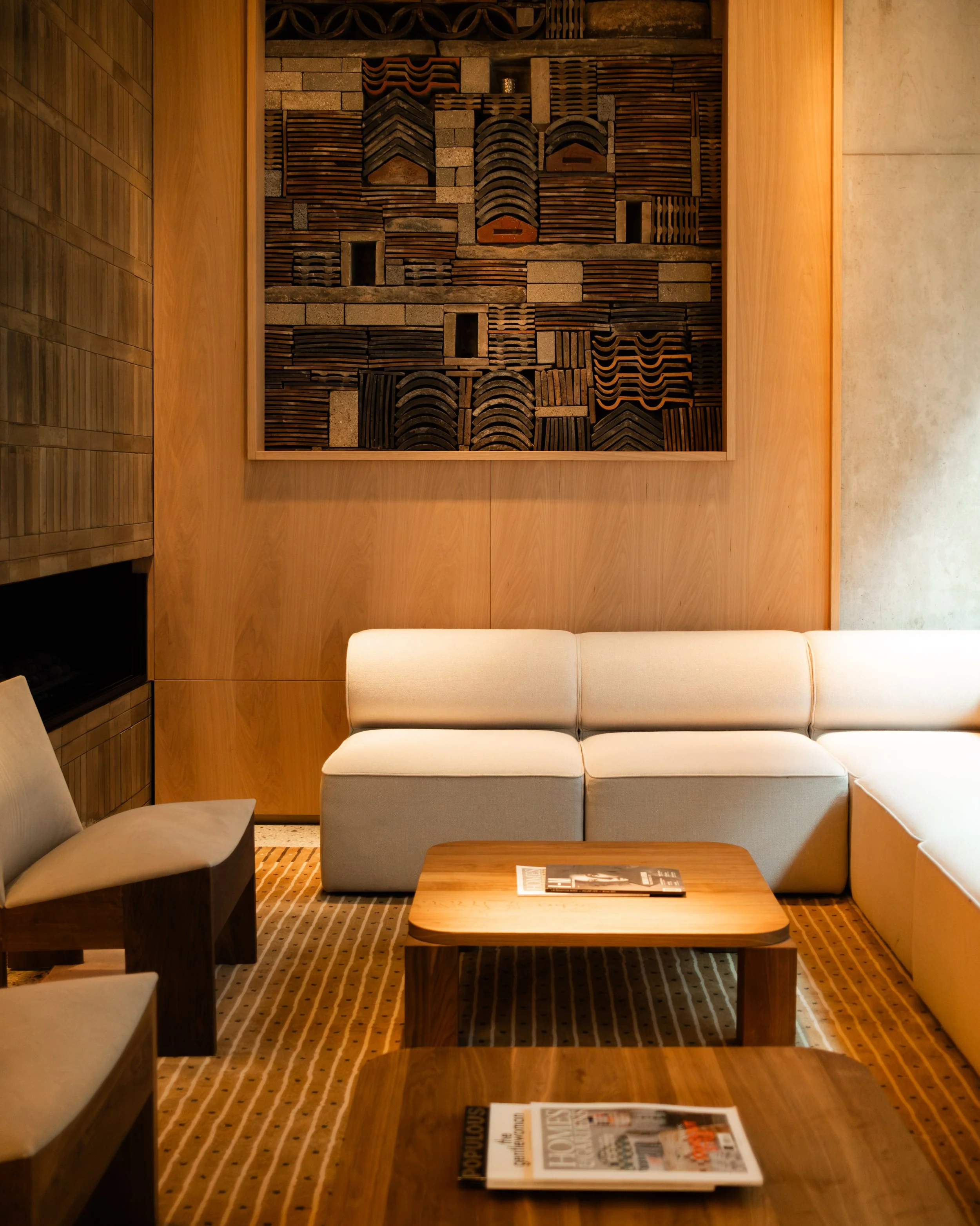 Hotel lobby with beige sectional sofa, wooden coffee tables with magazines, and wall art featuring wooden geometric patterns, warm lighting, and wooden and stone walls. Lionel Chu - Hotel & Travel Photographer