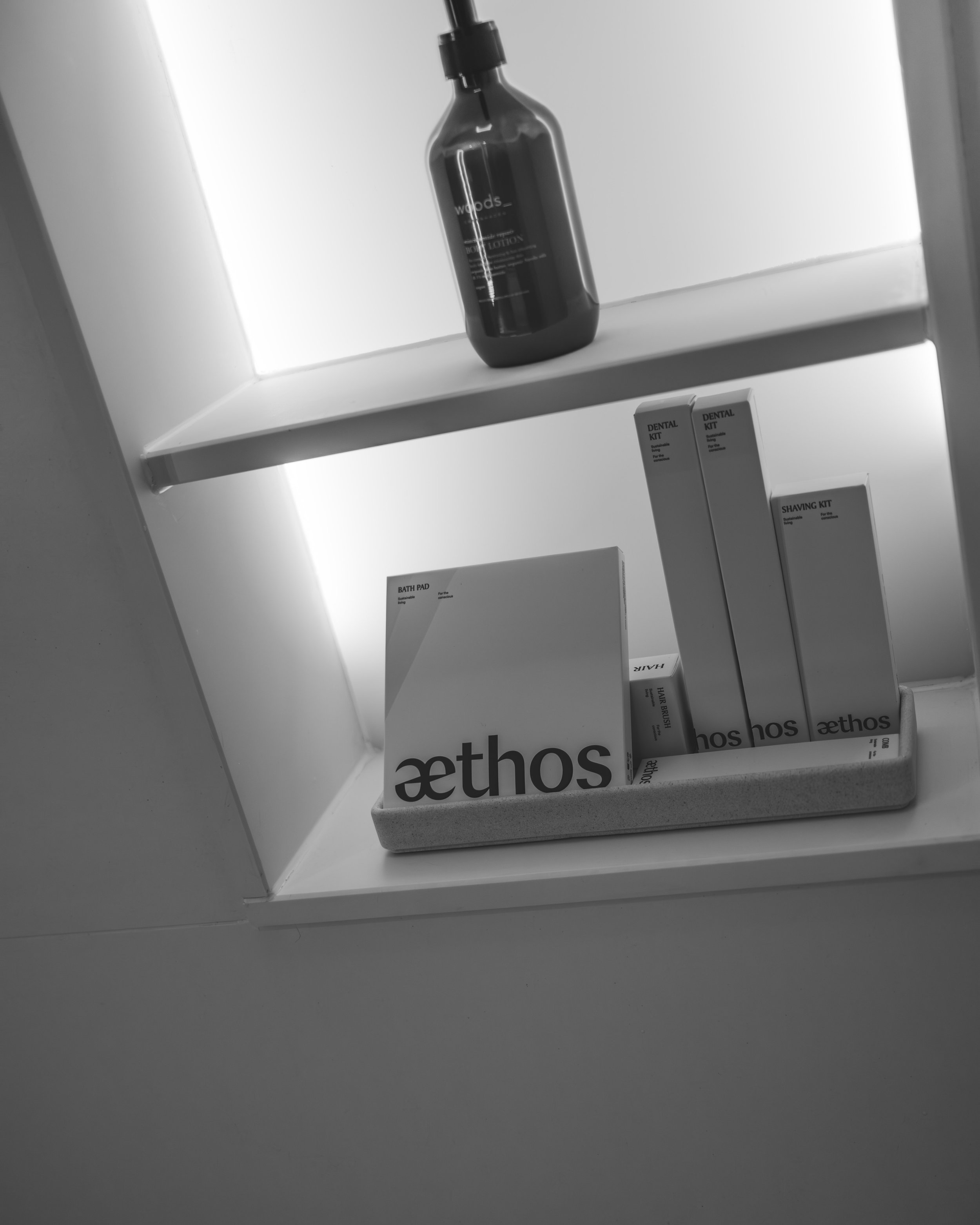 Black shelf with a spray bottle on top and boxes of dental products below, including a dental kit, a shaving kit, a bath pad, and hair brush.