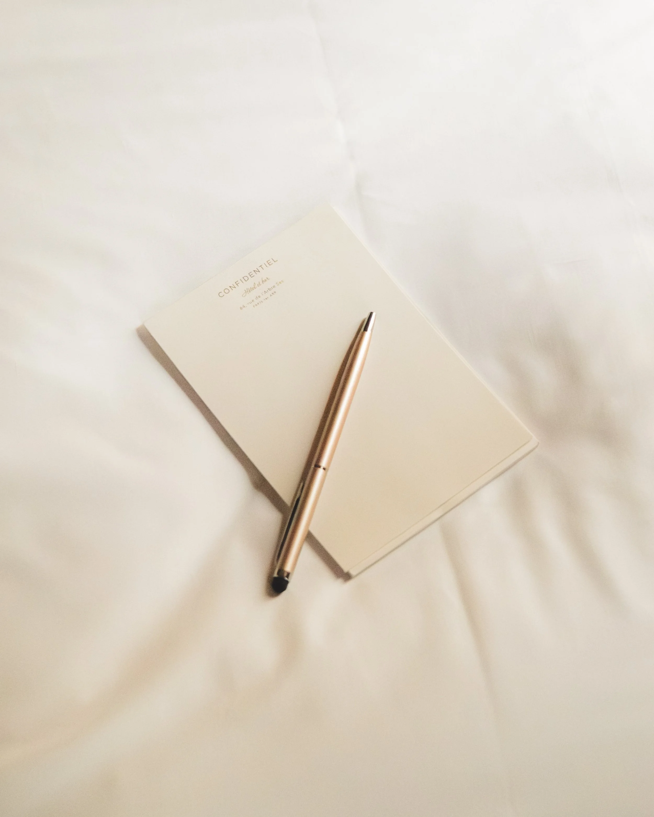 An open notebook with the word "CONFIDENTIEL" and some text in French, a rose gold pen, and a white background.