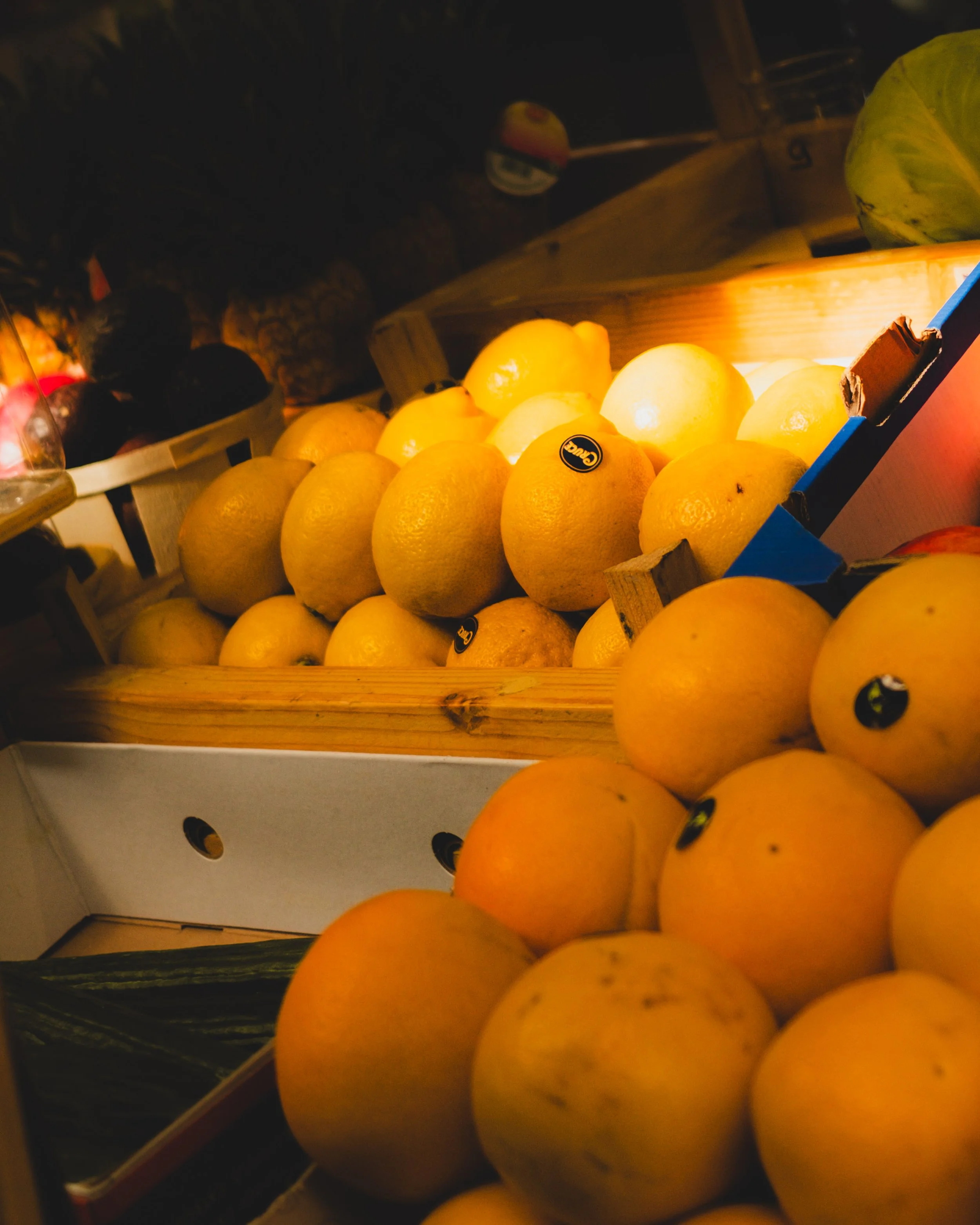 Lemons arranged in a wooden crate at a dimly lit produce store. Lionel Chu - Hotel & Travel Photographer.