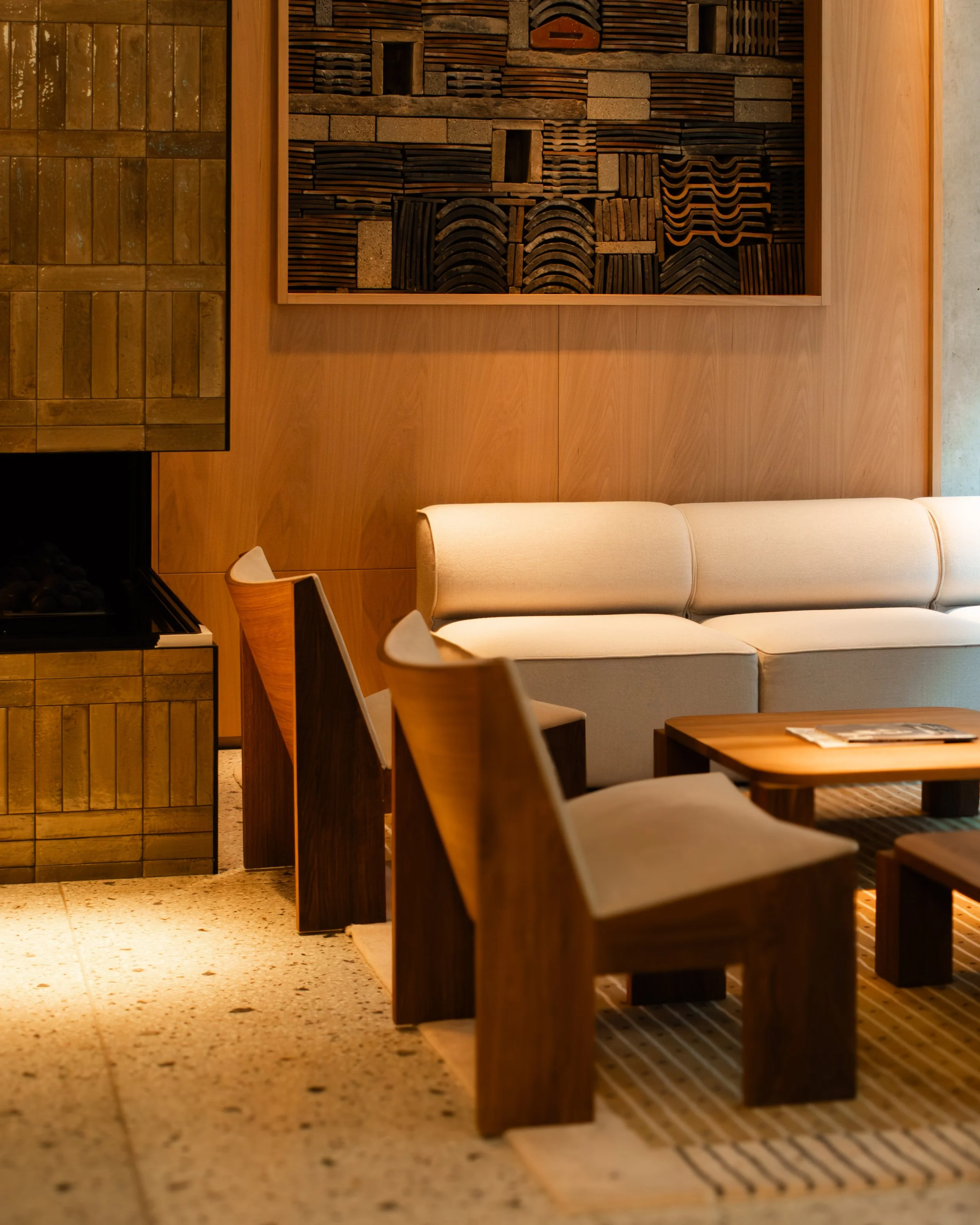 Hotel interior of a cozy lounge-lobby with beige sofa, wooden chairs, a wooden coffee table, and textured wooden decor on the wall. Lionel Chu - Hotel & Travel Photographer