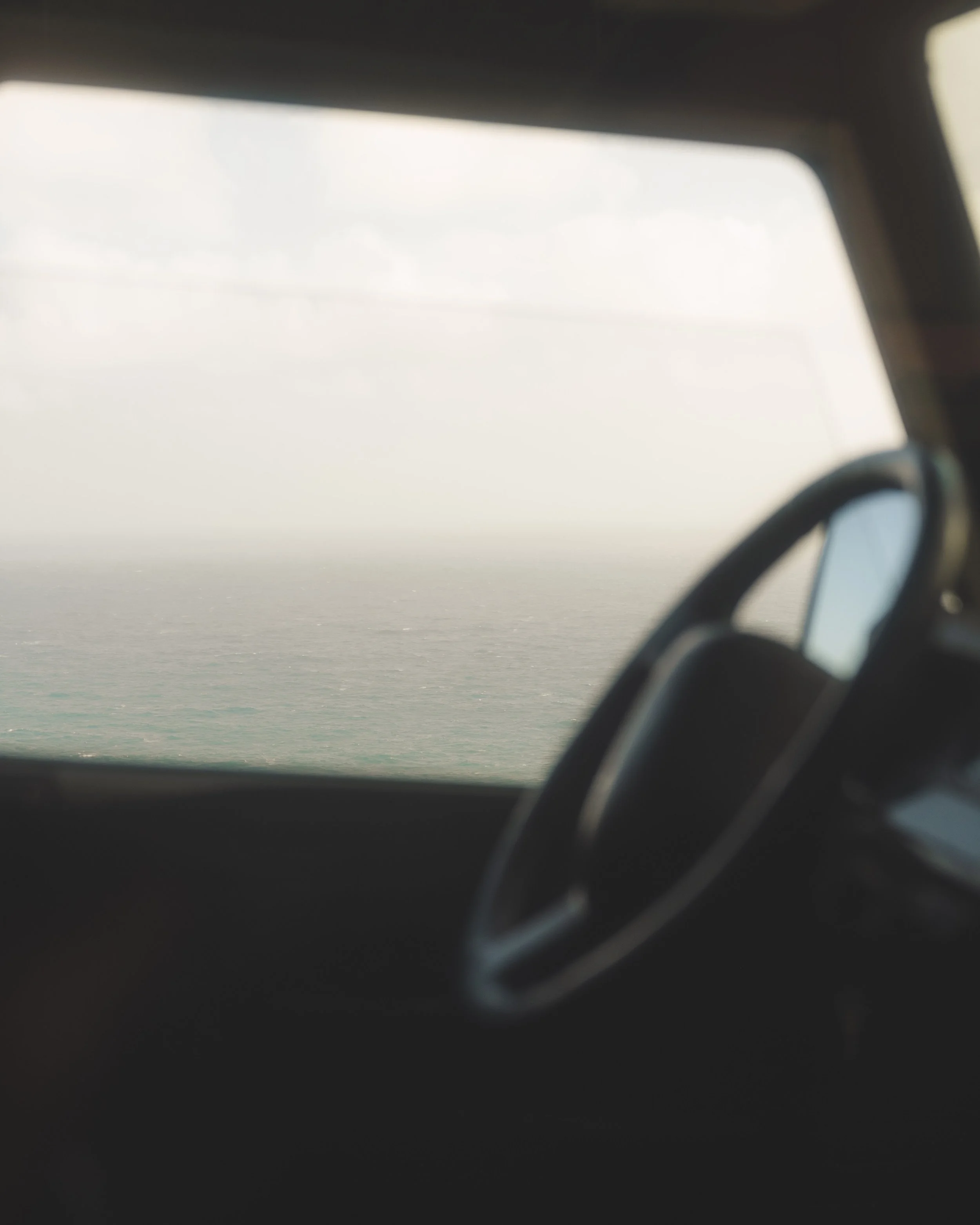 A close-up view of a side mirror of a vehicle reflecting the sky and clouds during sunset or sunrise, with a partial view of the car's window and interior.