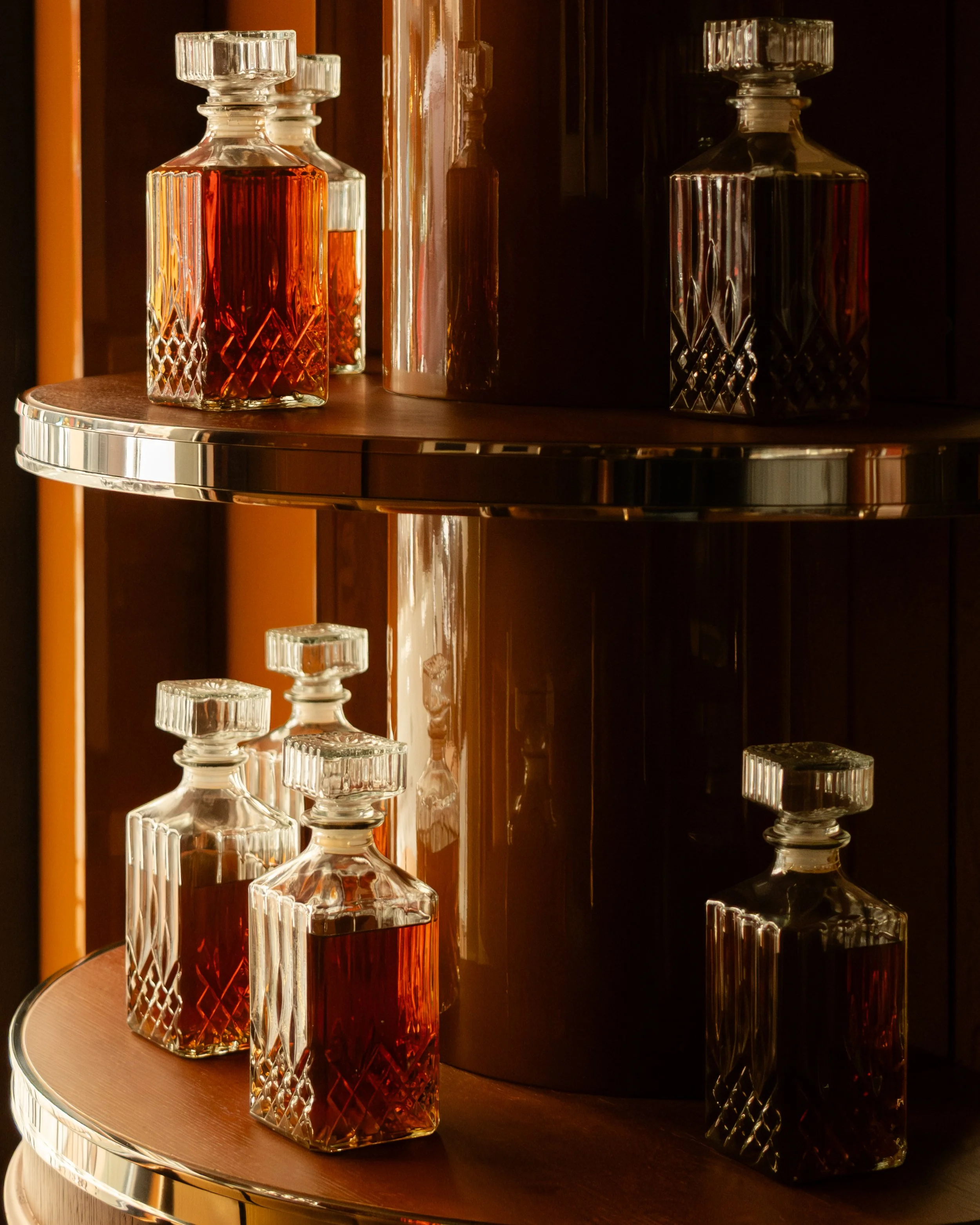 Decorative glass decanters filled with amber-colored liquid on a round wooden and metal shelf. Lionel Chu - Hotel & Travel Photography