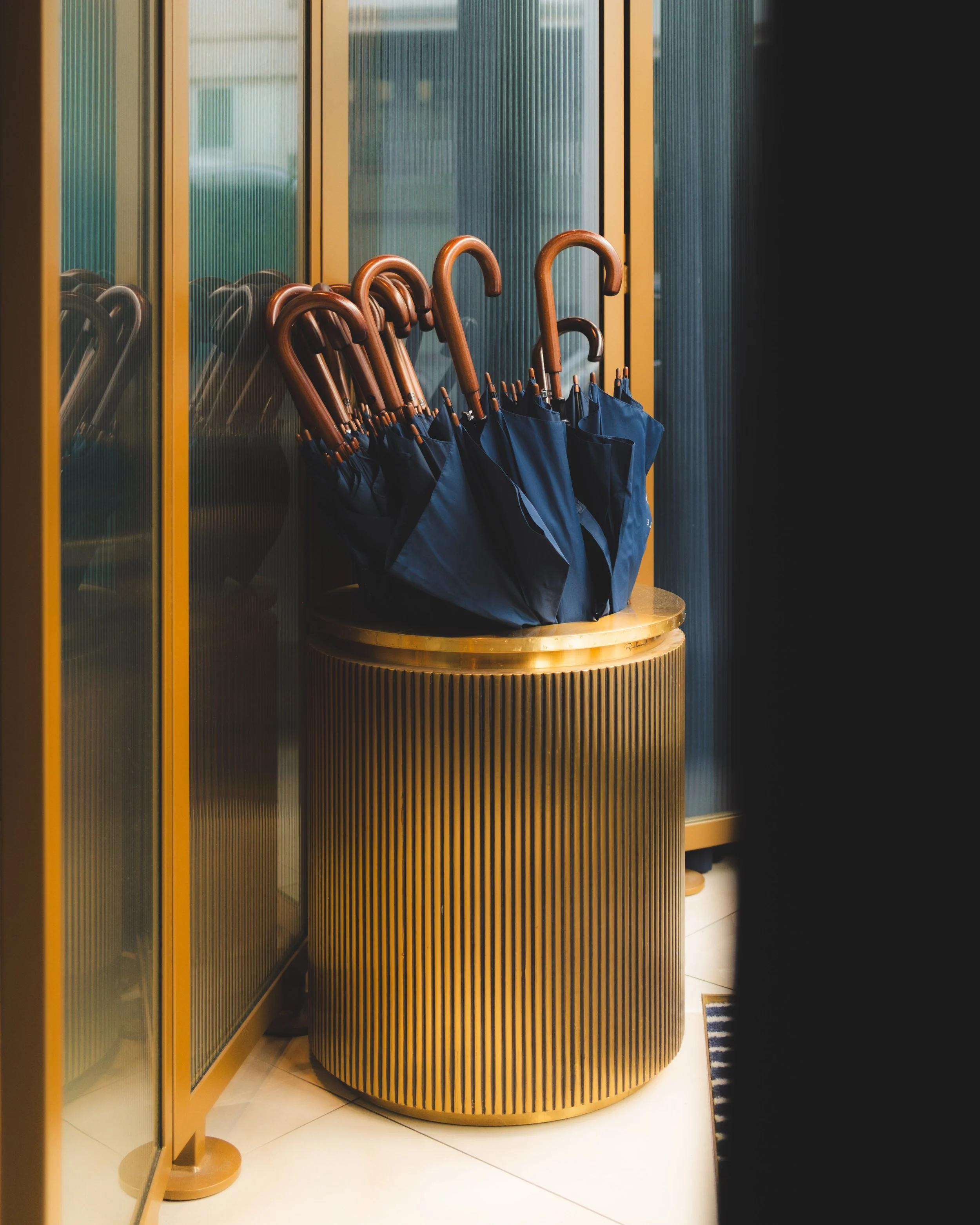 A display of black umbrellas with wooden handles arranged in a semi-circle behind a yellow wooden partition with vertical slats in a store or office setting.
