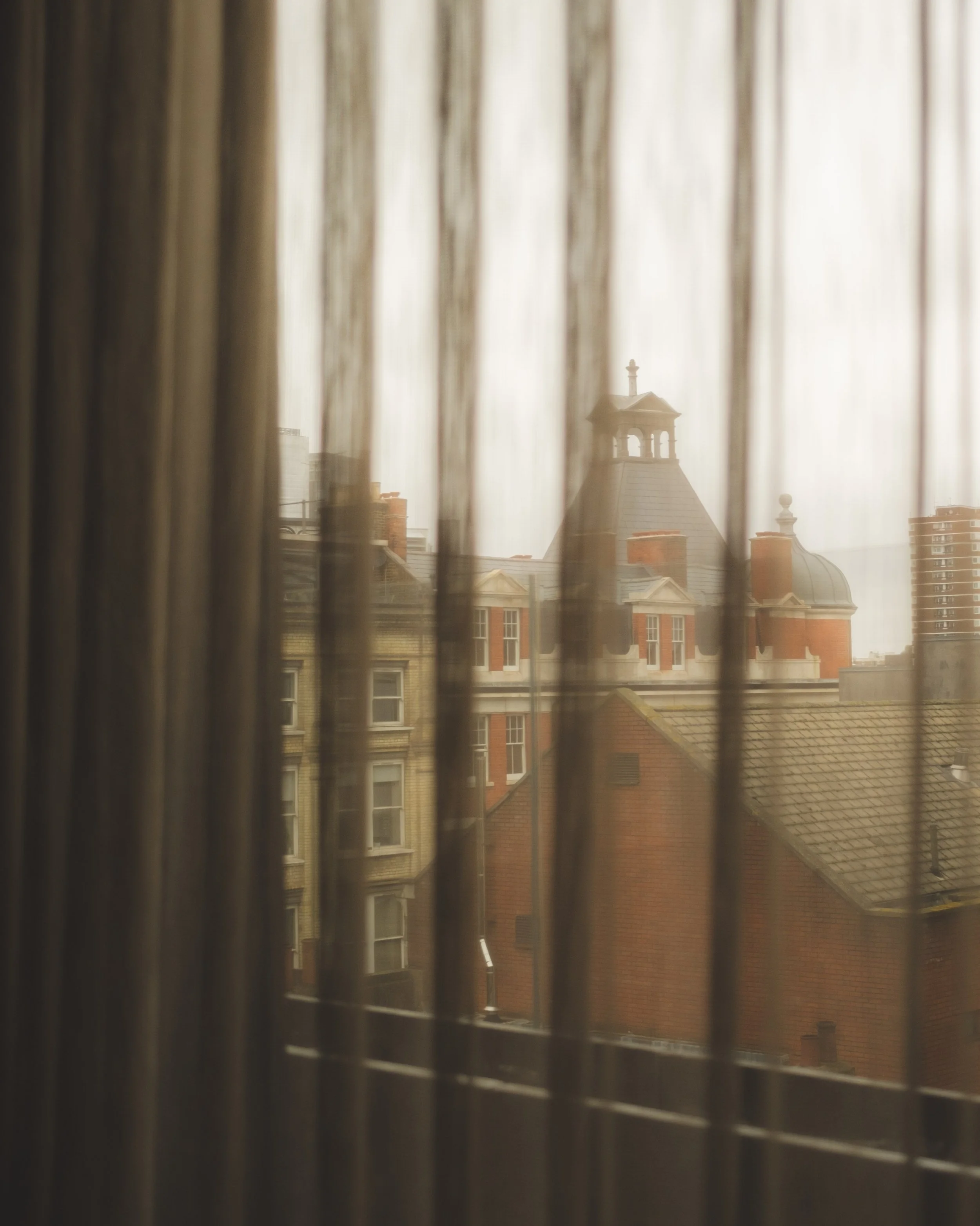 View of rooftops and a church steeple seen through bathroom window with blinds.