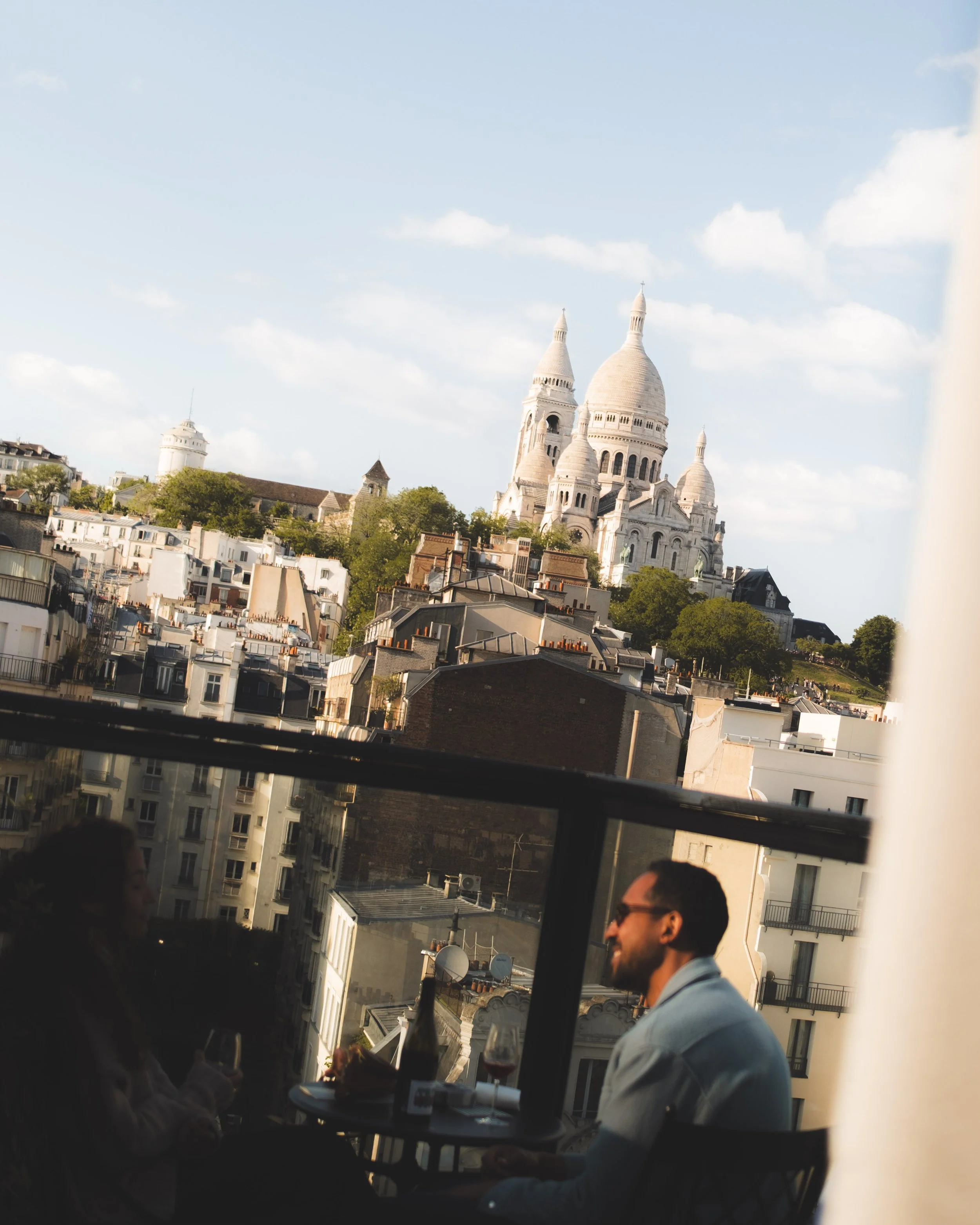 People dining outdoors on a terrace with a view of the Sacré-Cœur Basilica in Paris.