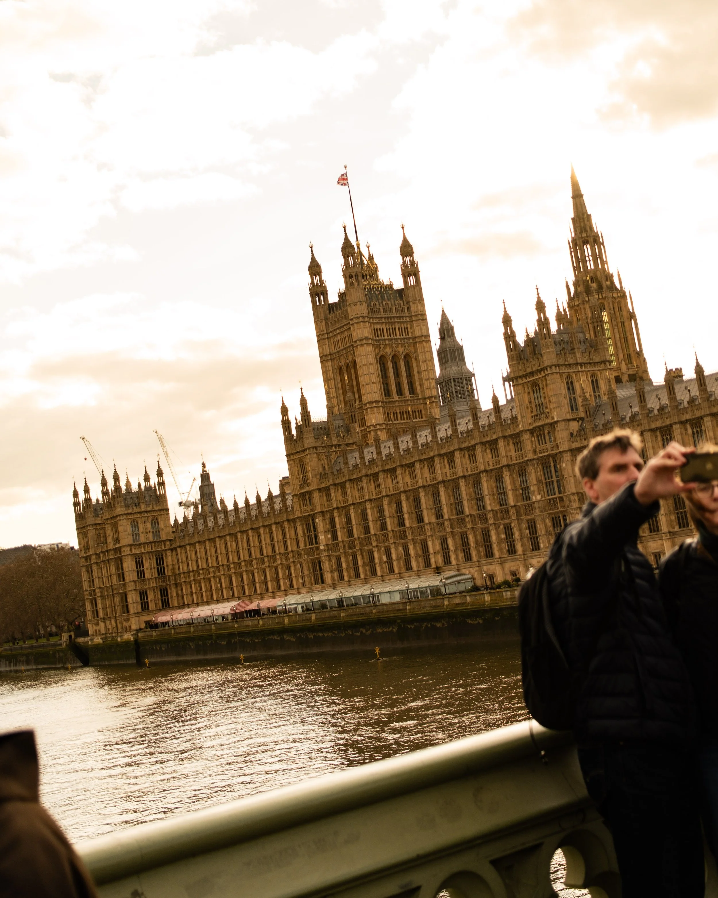 Historical Palace of Westminster in London seen from a bridge over the River Thames, with people taking photos in the foreground, during sunset. Lionel Chu - Hotel & Travel Photographer