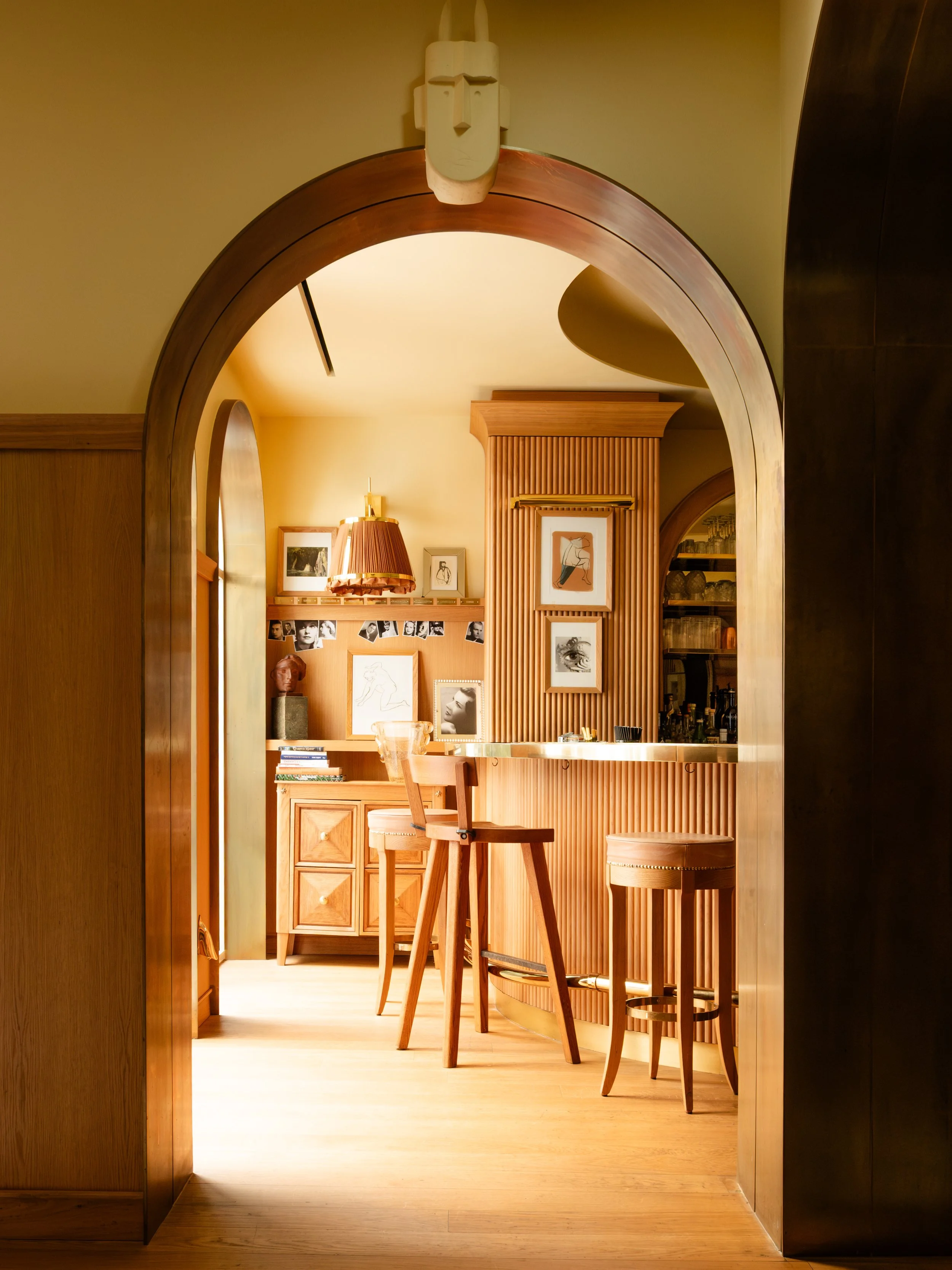 Interior view through a wooden arched doorway showing a cozy room with wooden furniture, framed artwork on the wall, and a bar area with bar stools. Lionel Chu - Hotel & Travel Photography