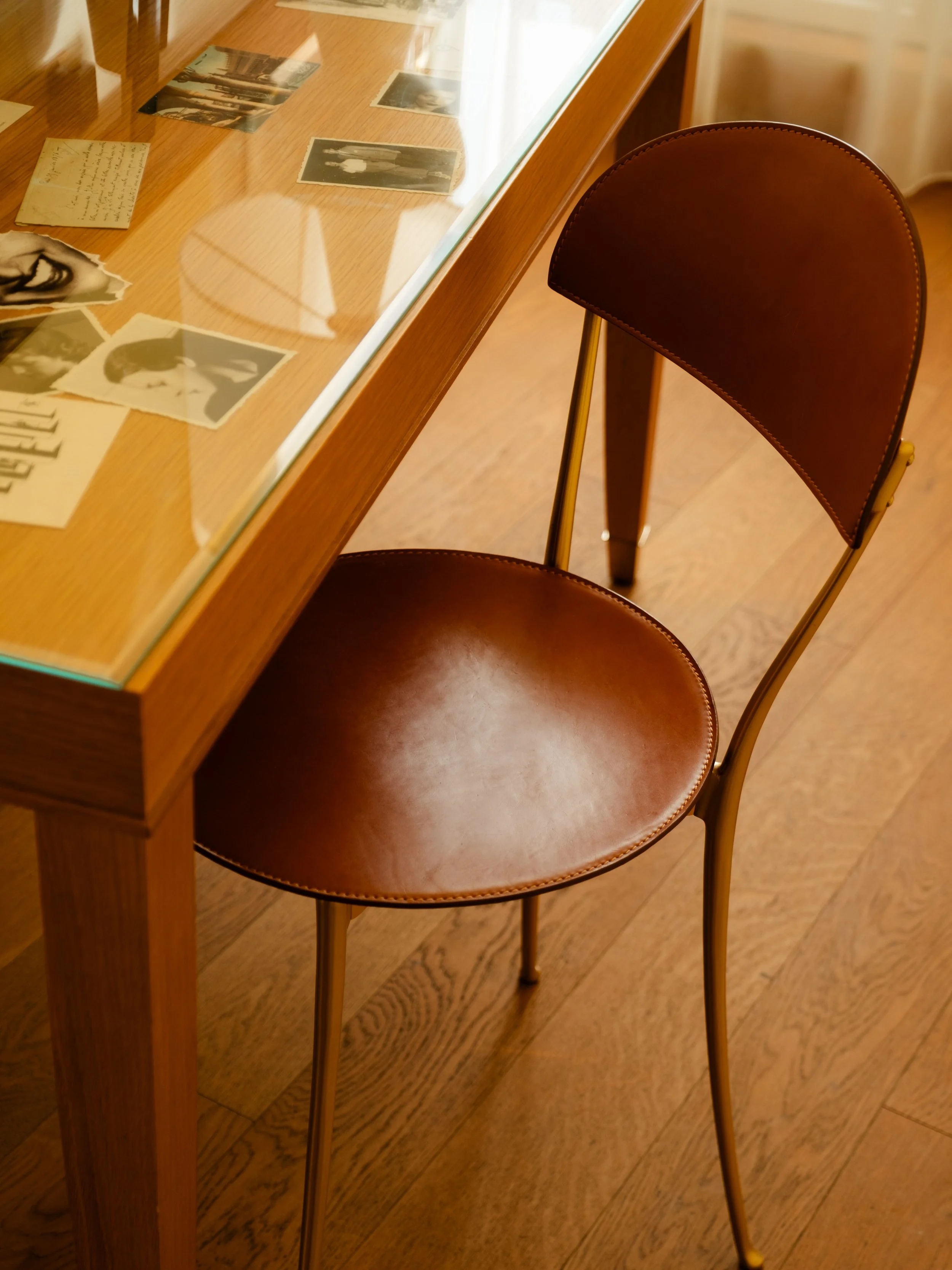 A brown leather seat chair next to a wooden and glass display table with historical photographs and handwritten notes inside. Lionel Chu - Hotel & Travel Photography