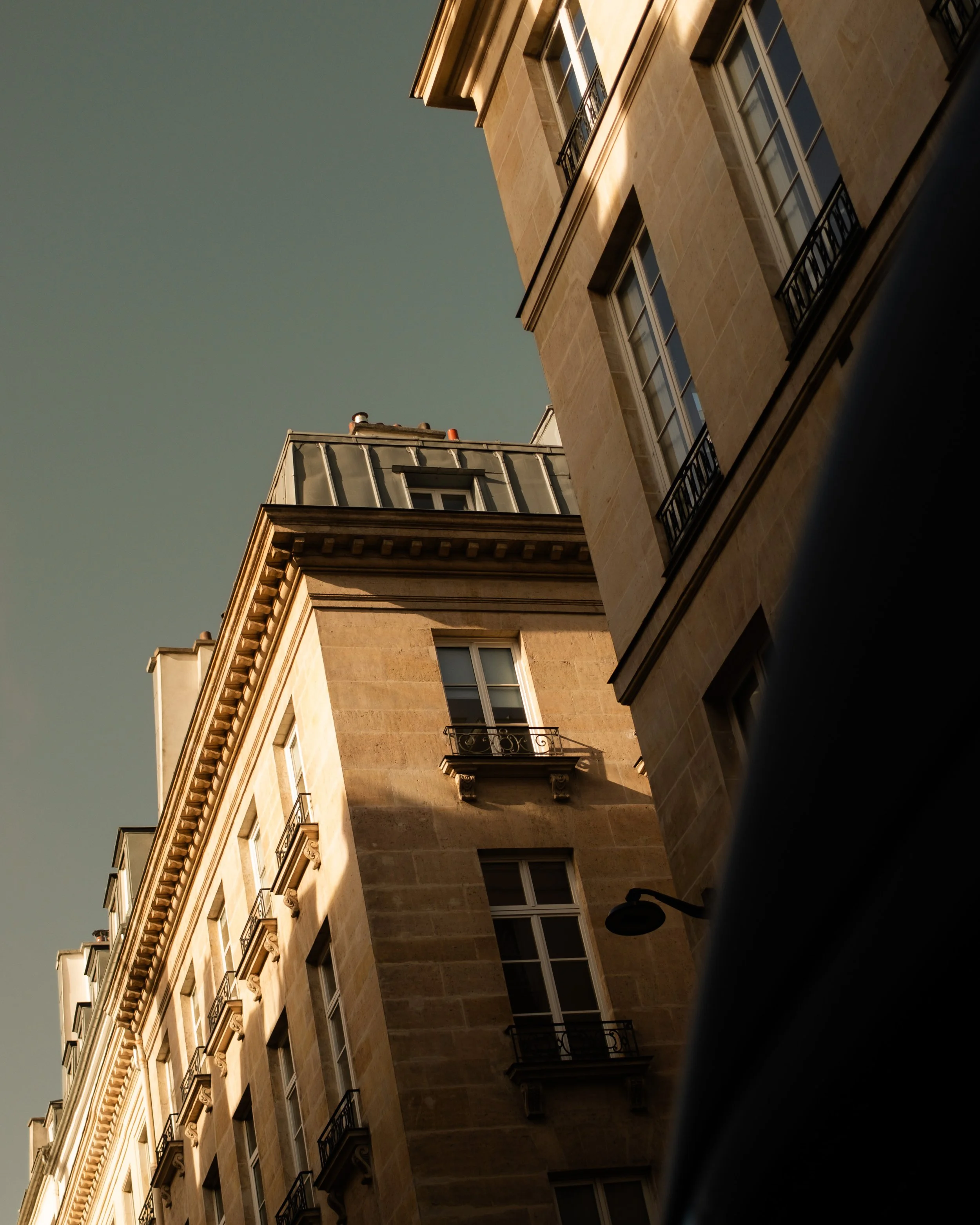 View of a European-style building from below, displaying windows with small balconies and decorative architectural details, with a clear sky in the background. Lionel Chu - Hotel & Travel Photographer