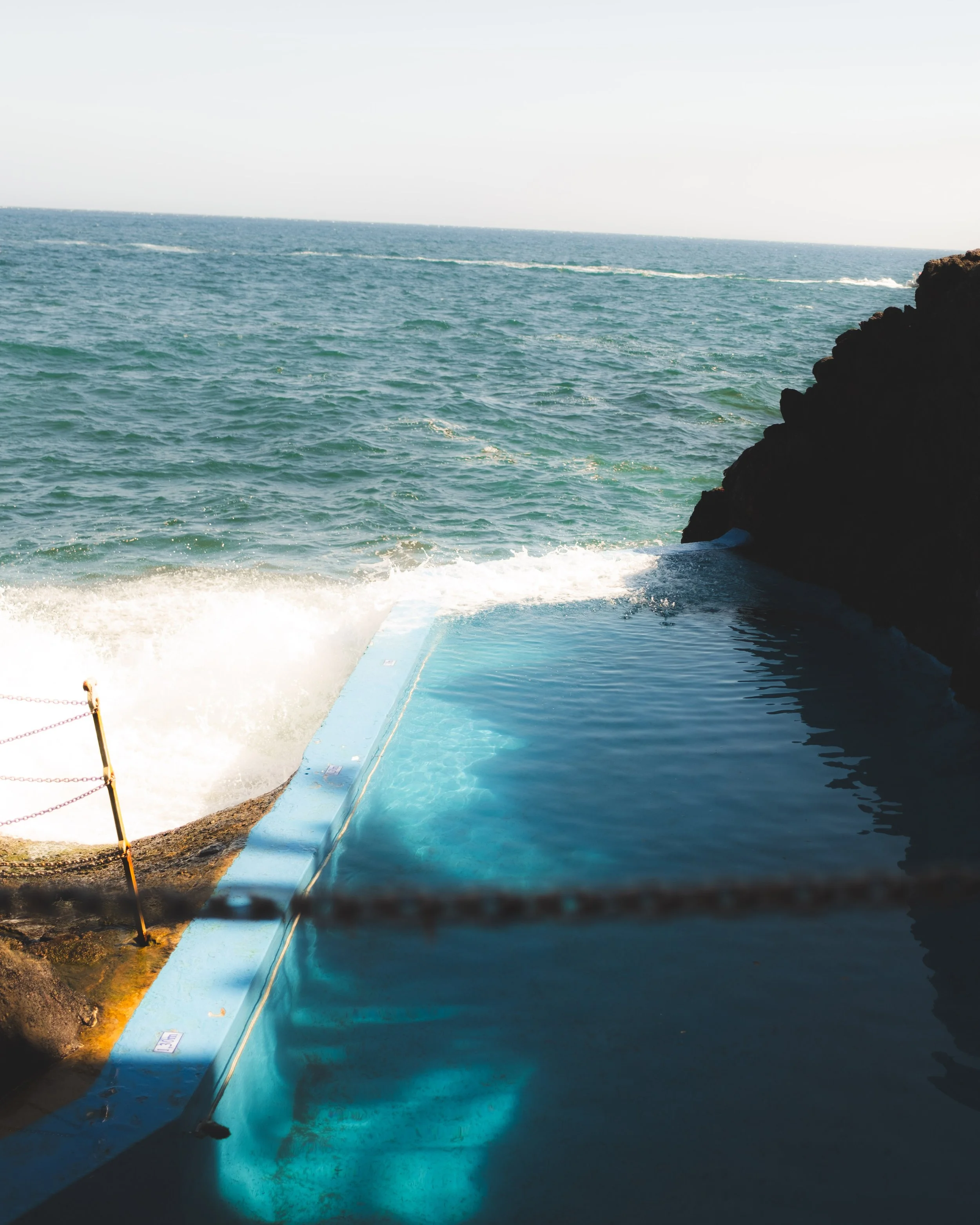 View of the ocean with a rocky shoreline on the right, a partially submerged blue platform or boat, and a rope with a yellow pole on the left.