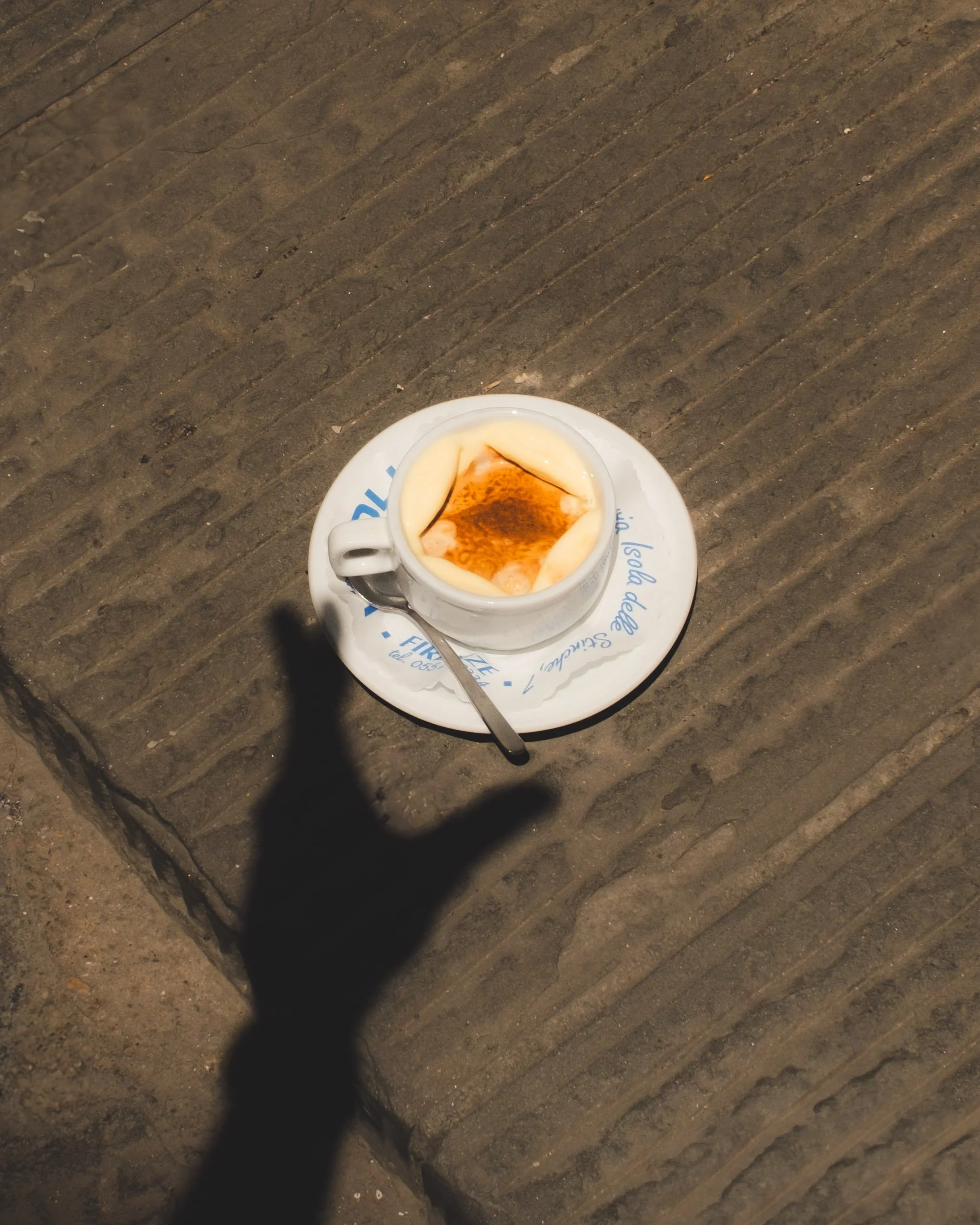A cup of affogato, placed on a saucer with a spoon, on a textured wooden surface, with a shadow of a hand nearby. Lionel Chu - Hotel & Travel Photographer