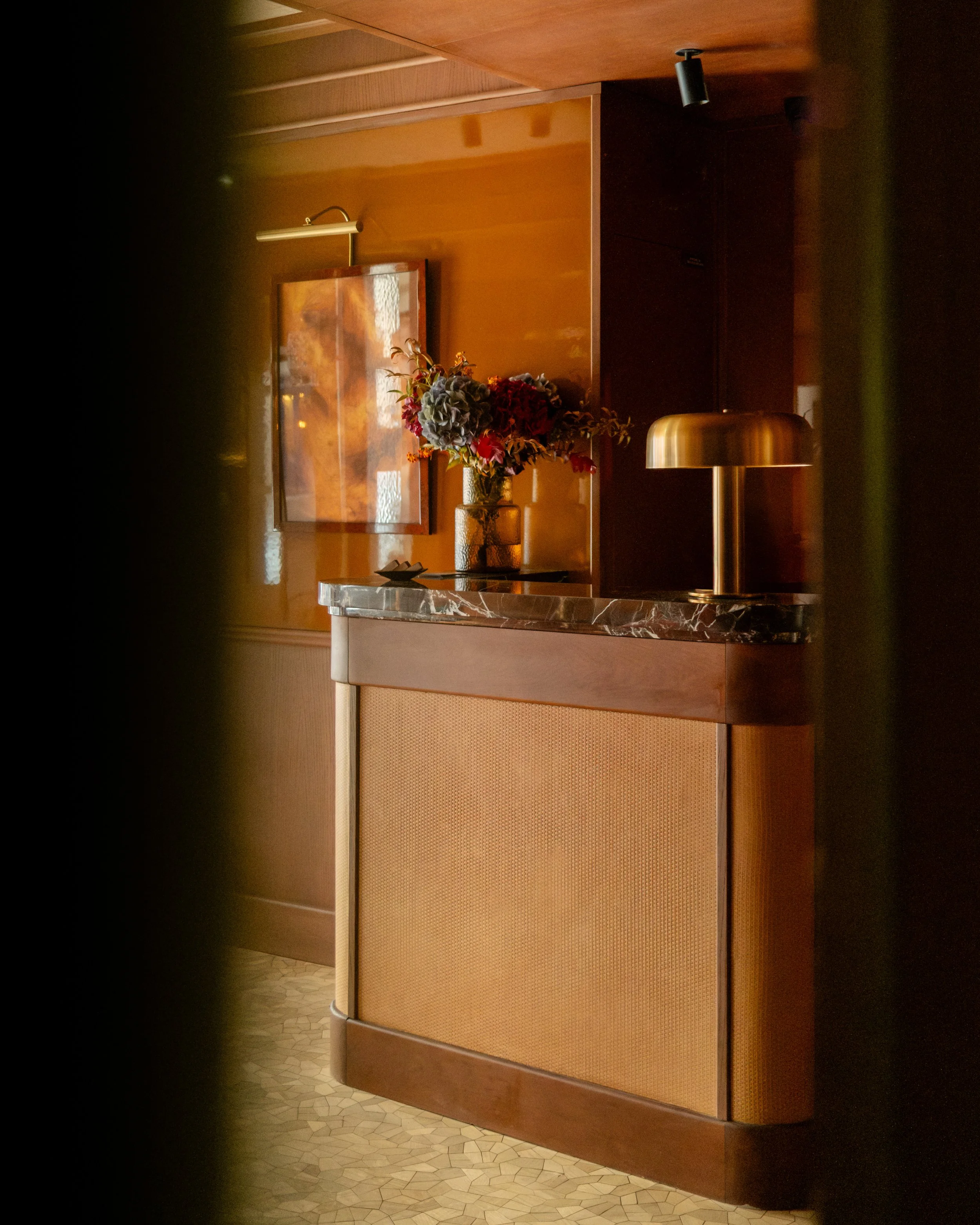 Interior hotel lobby or reception area with wooden walls, a marble-topped counter, a vase with colorful flowers, a framed artwork, a gold lamp, and track lighting. Lionel Chu - Hotel & Travel Photography