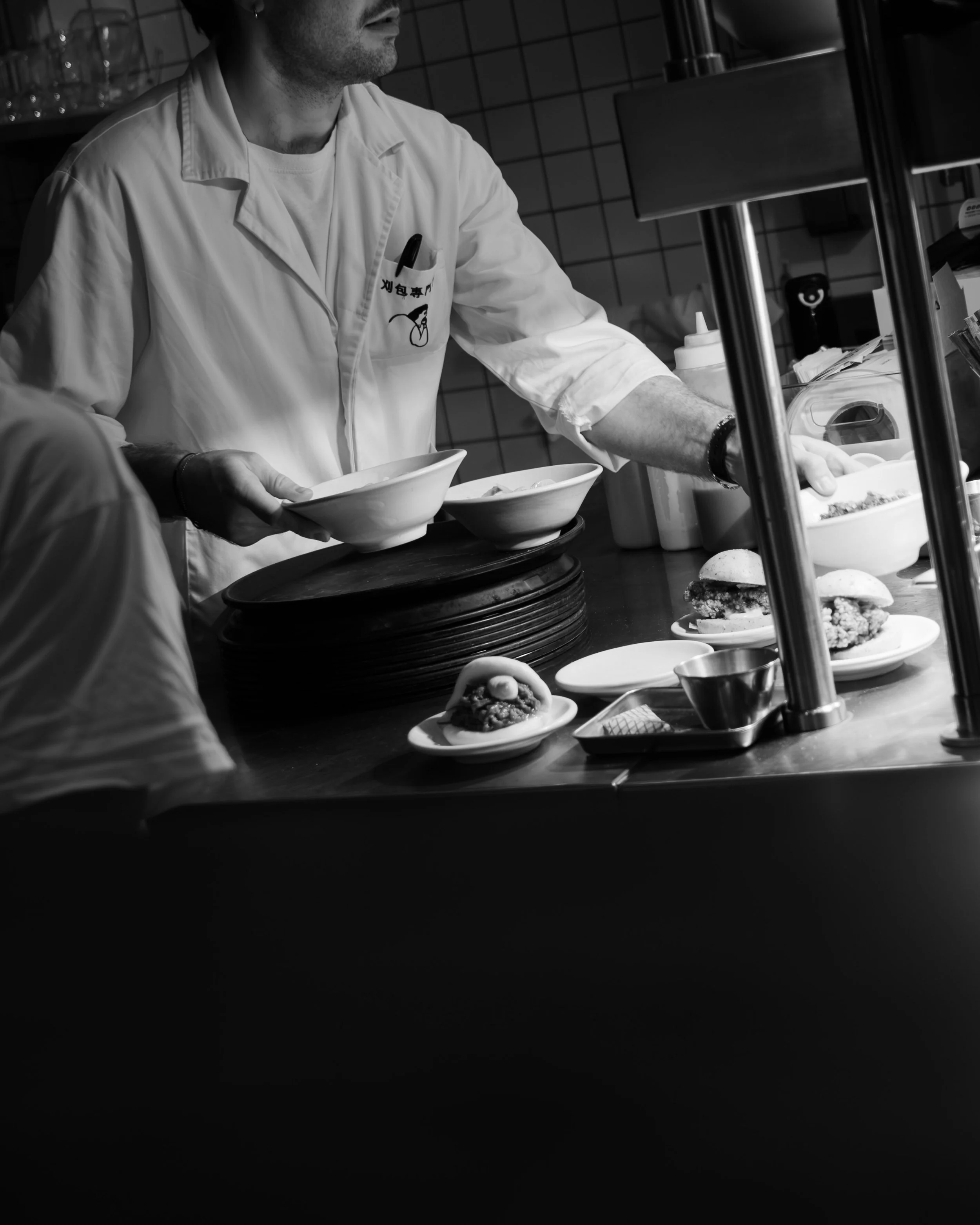 A chef preparing food behind a counter with plates of burgers and bowls, with condiments and kitchen utensils visible. Lionel Chu - Hotel & Travel Photographer