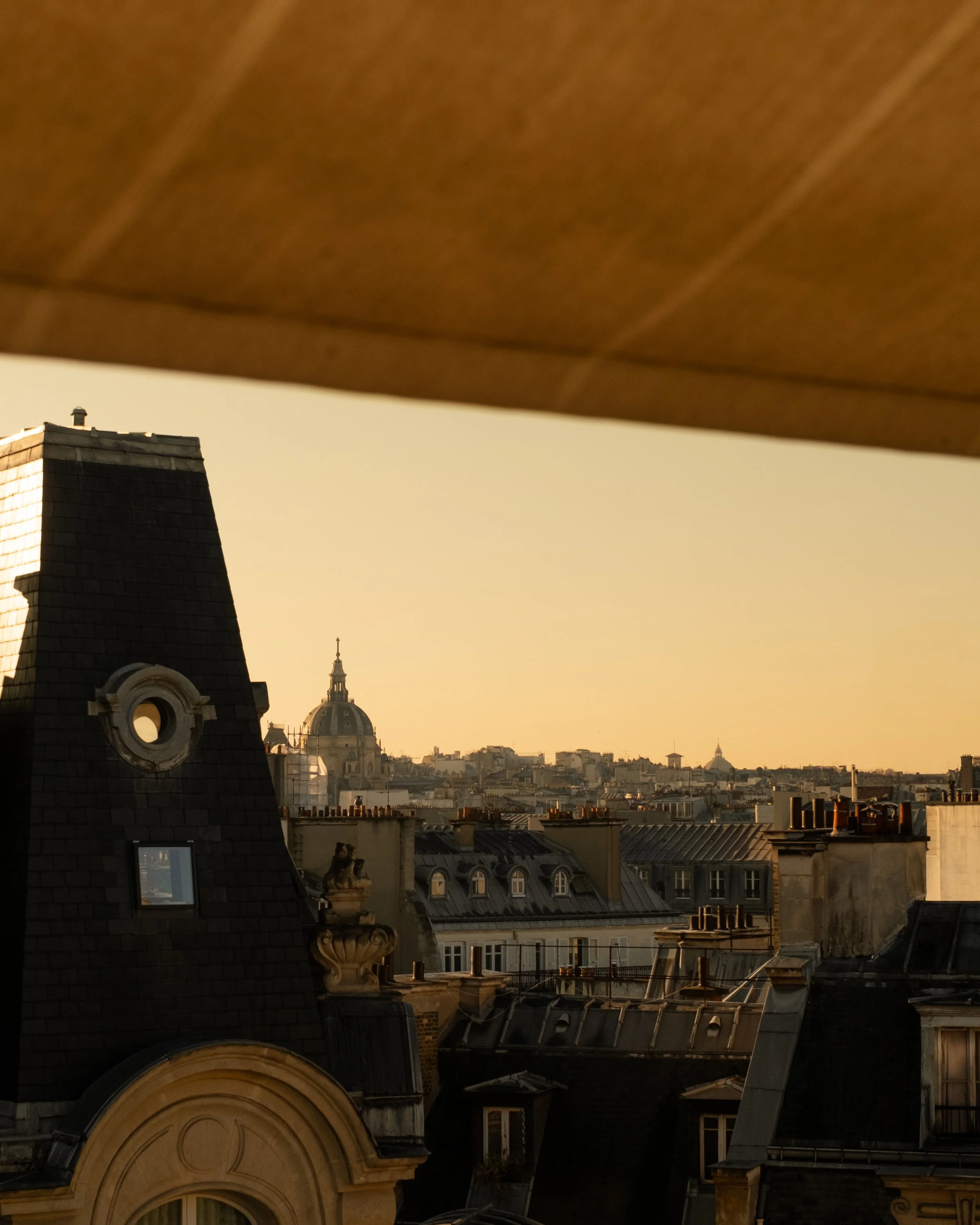 View of Paris rooftops at sunset with domed building in the distance and a rooftop with chimneys in the foreground. Lionel Chu - Hotel & Travel Photographer