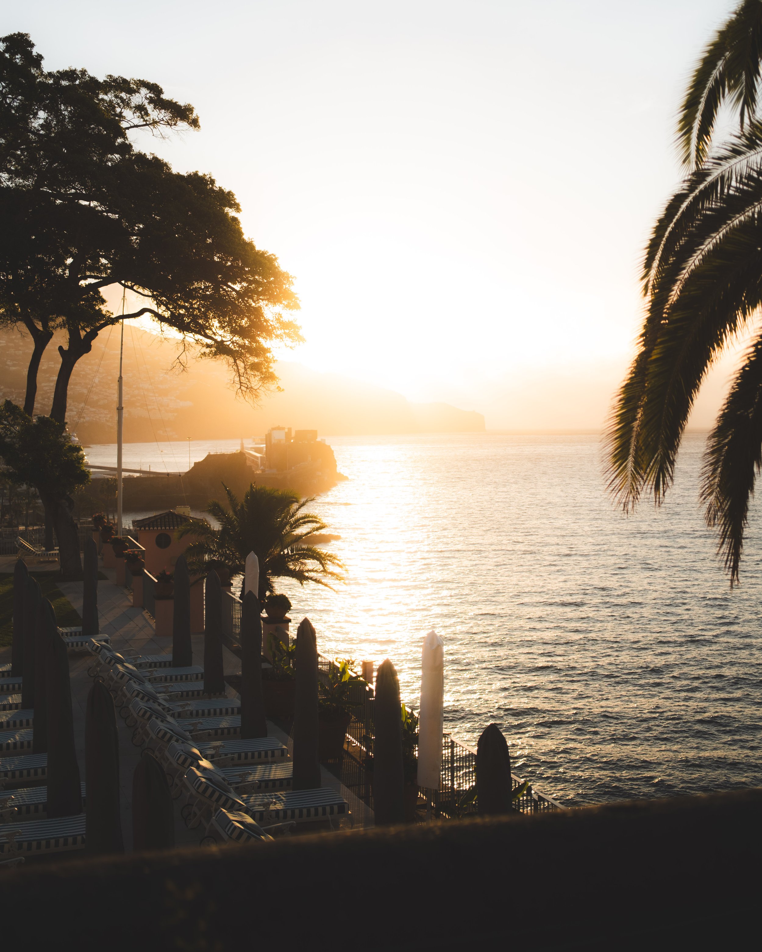 Sunset over a body of water with trees and a deck with lounge chairs and umbrellas in the foreground.