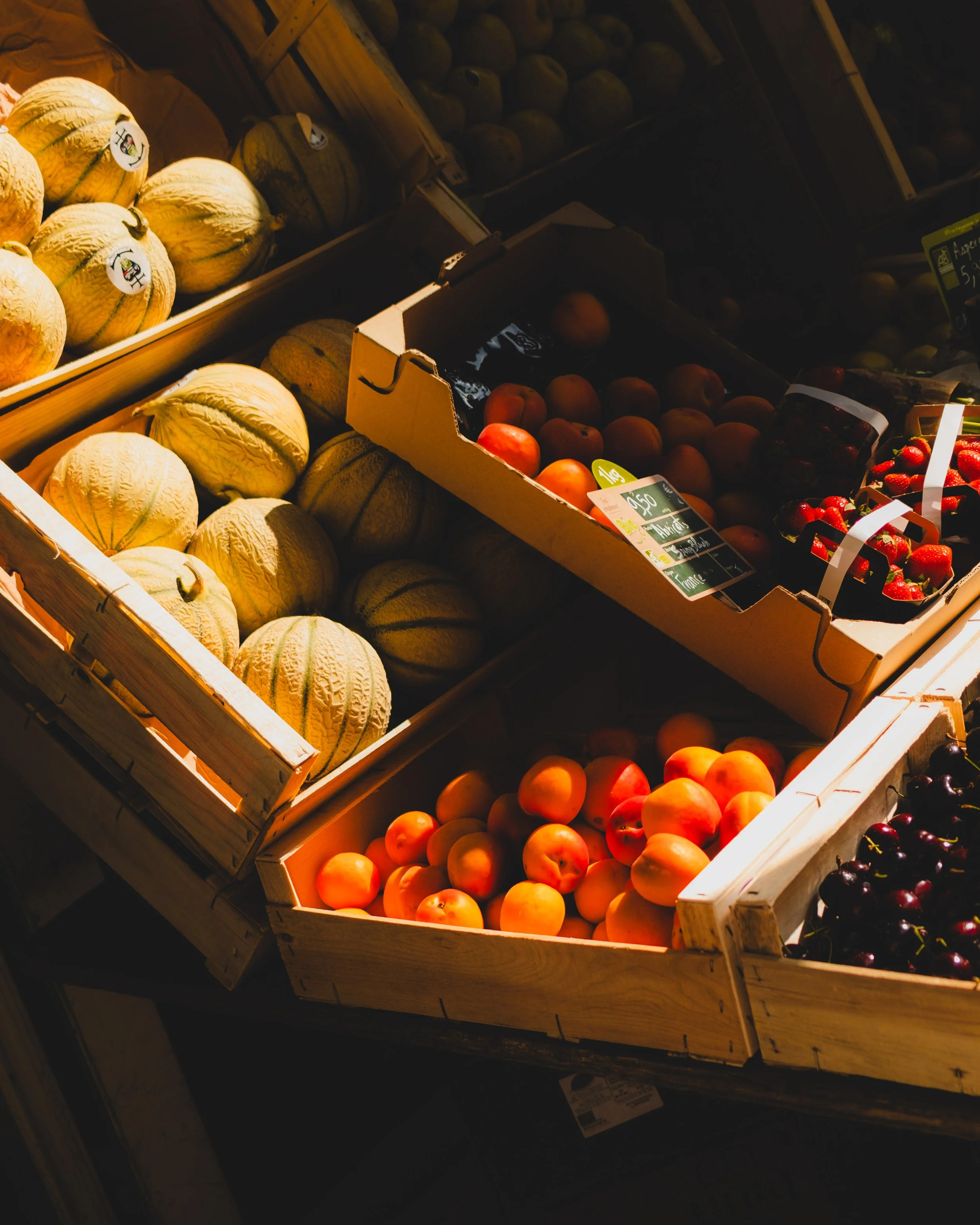 Various fruits displayed in wooden crates at a grocery store, including cantaloupe, apricots, strawberries, and cherries. Lionel Chu - Hotel & Travel Photographer