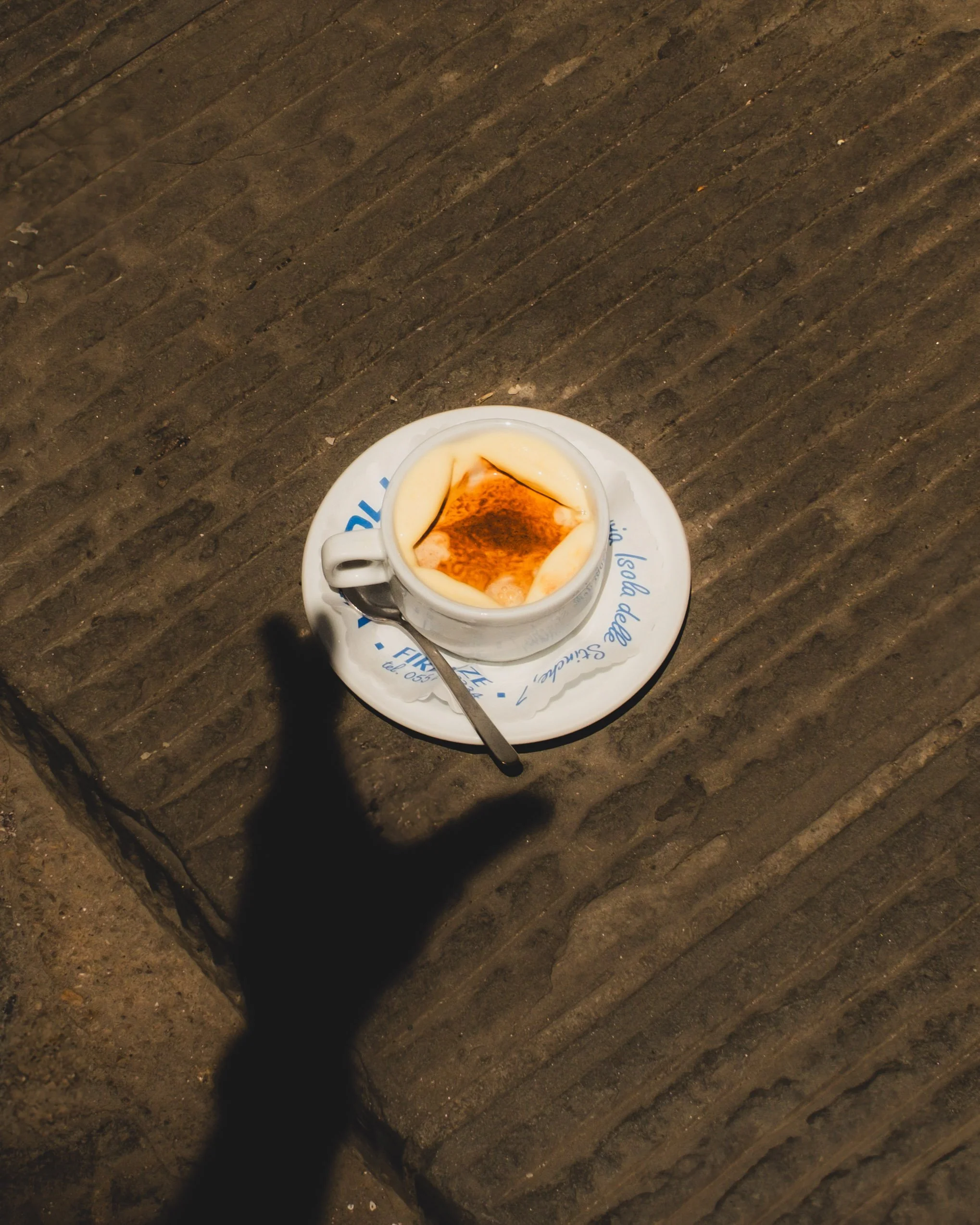 A cup of affogato, placed on a saucer with a spoon, on a textured wooden surface, with a shadow of a hand nearby. Lionel Chu - Hotel & Travel Photographer