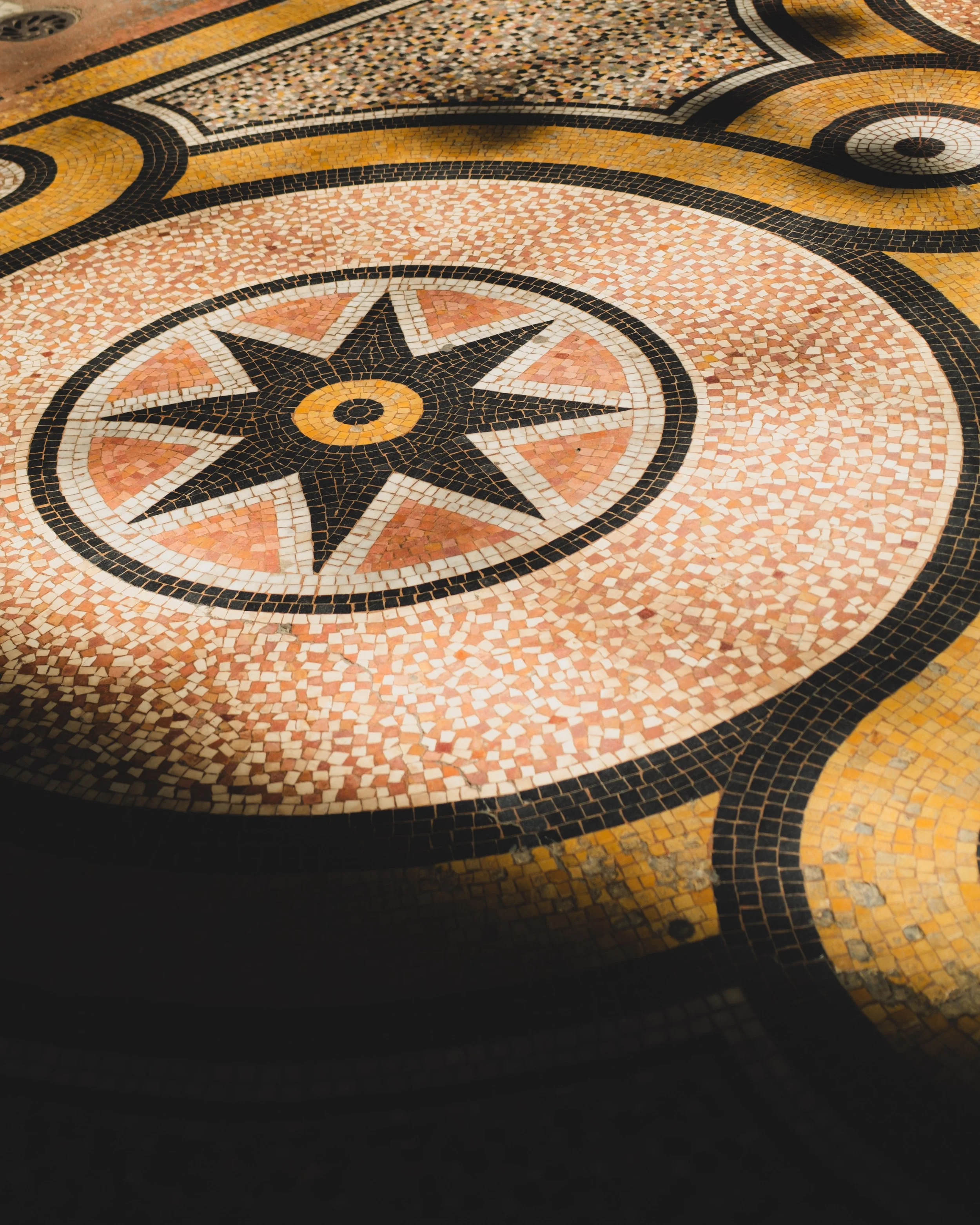 Decorative mosaic tile floor with a compass rose design in black, white, yellow, and red tiles. Lionel Chu - Hotel & Travel Photographer