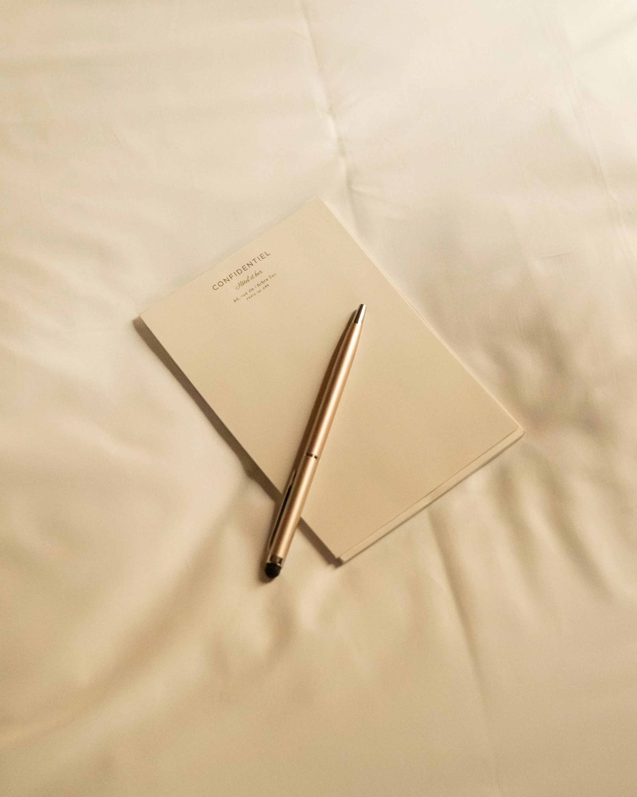 A notebook titled CONFIDENTIEL with a pen resting on it, on a white surface. Lionel Chu - Hotel & Travel Photography