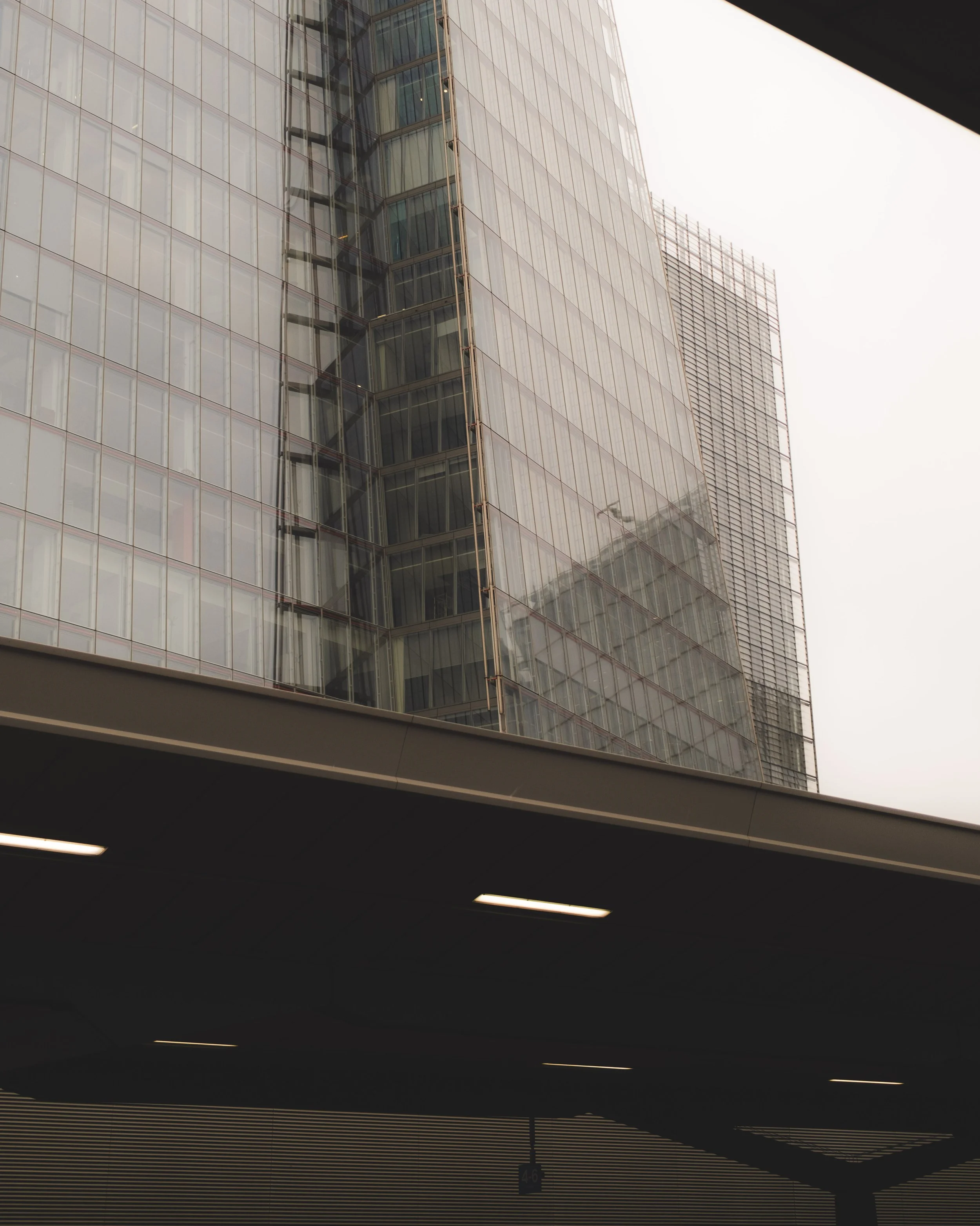 View of a tall glass skyscraper building with reflective windows, seen through a window frame, in an overcast setting.