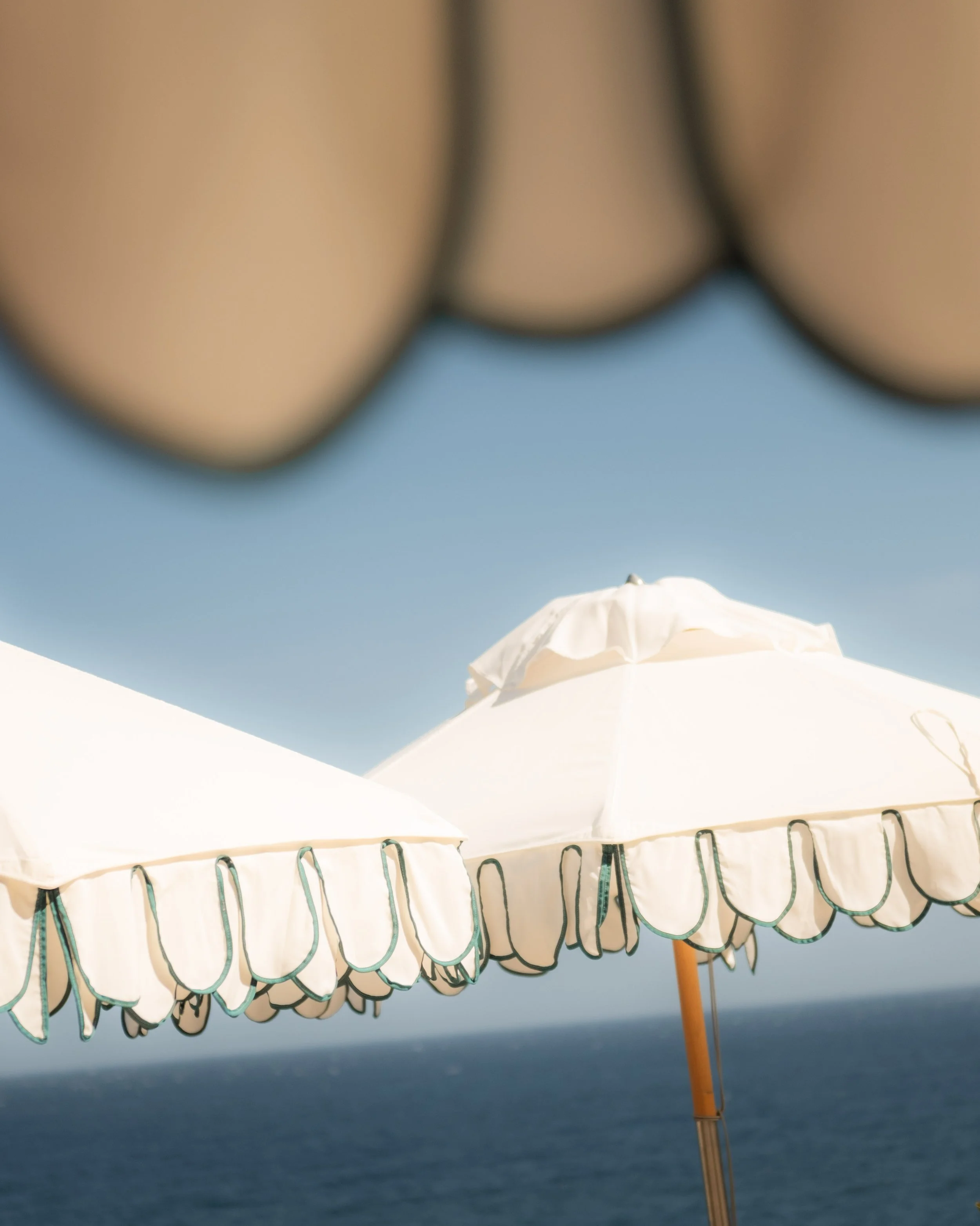 Close-up view of a white beach umbrella with scalloped edges and decorative trim, set against a clear blue sky at the beach.