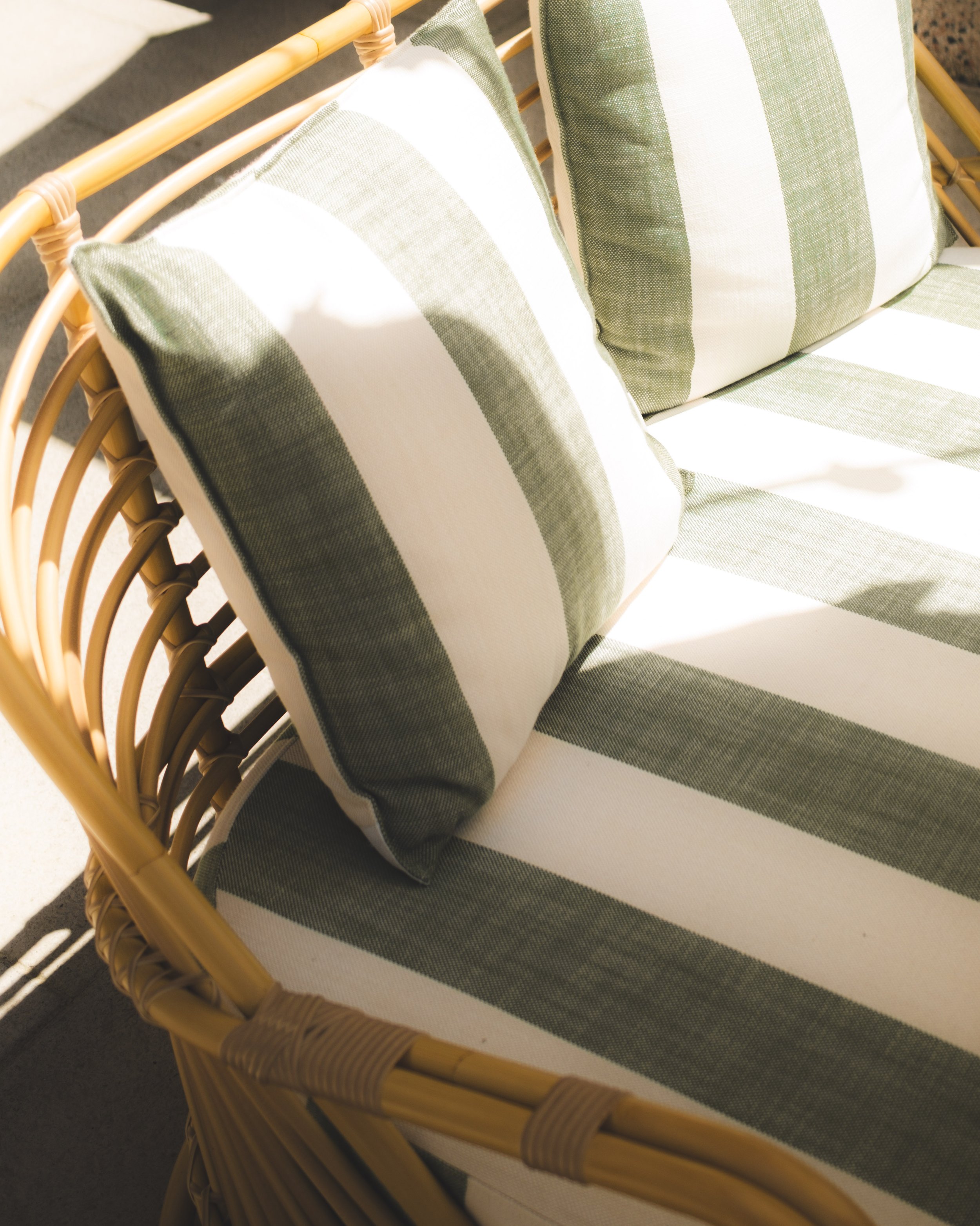 Close-up of a bamboo outdoor furniture piece with a cushion featuring green and white stripes.