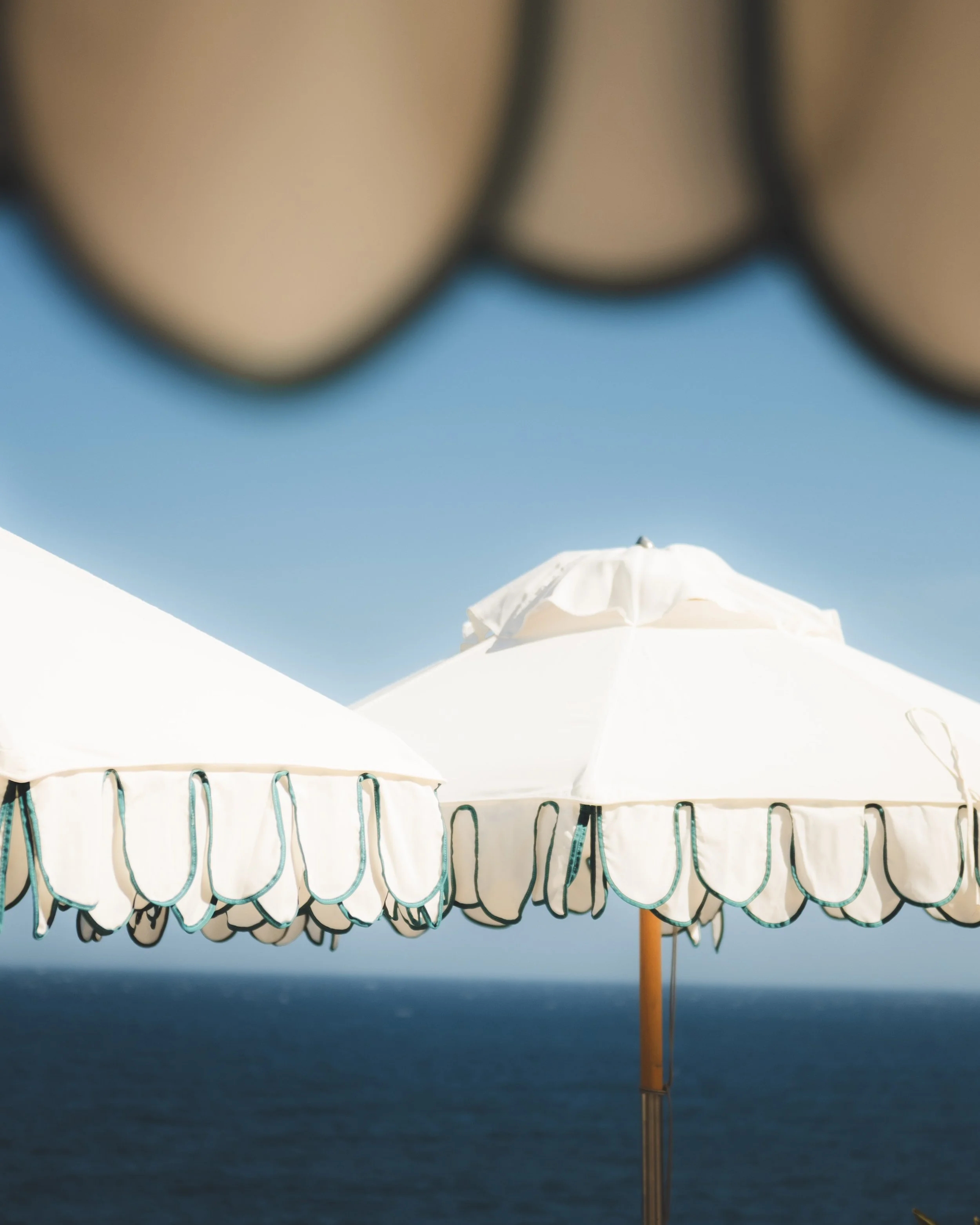Beach umbrella with blue and white scalloped trim in front of the ocean under a blue sky.