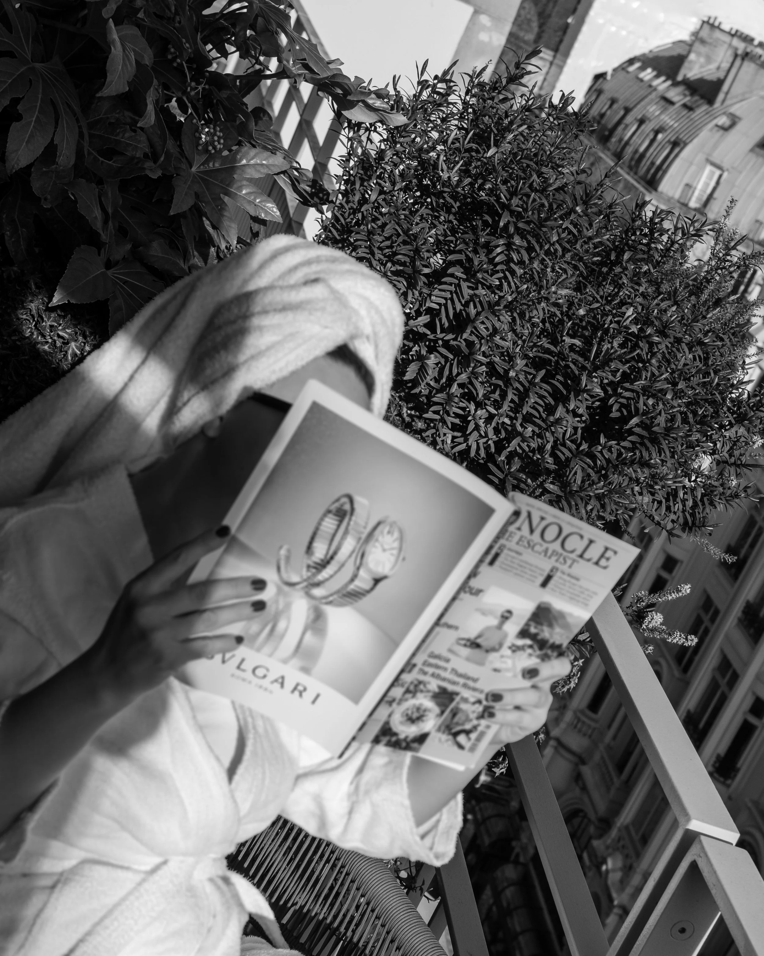 Person reading a magazine on a balcony with plants and city buildings in the background. Lionel Chu - Hotel & Travel Photographer