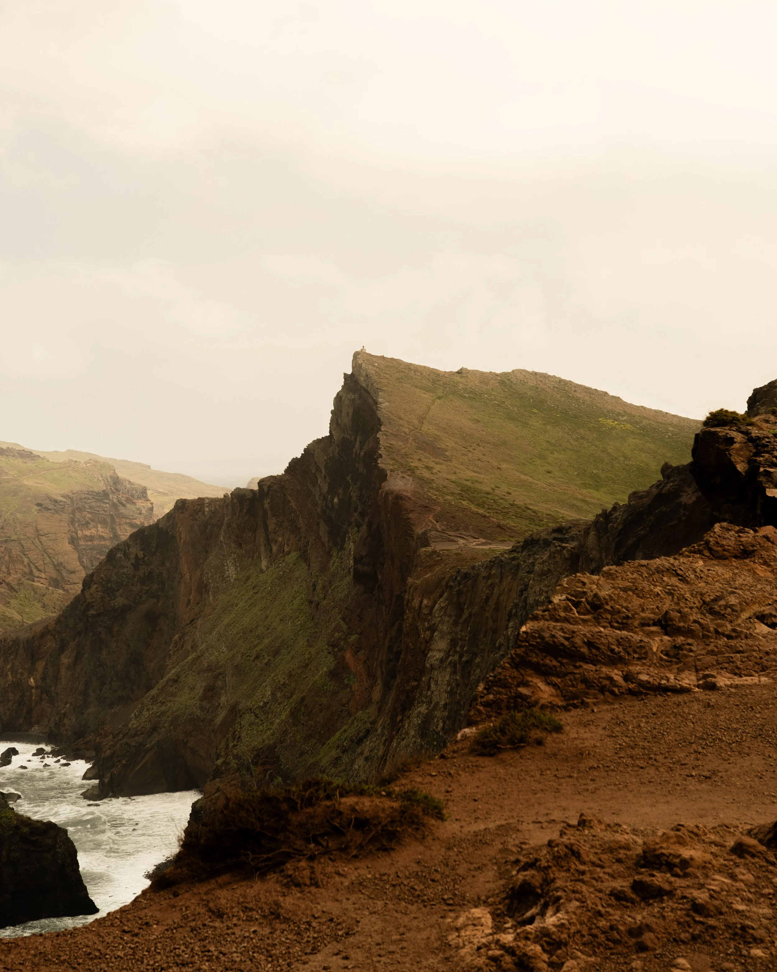 Cliffside landscape with grassy slopes, rocky formations, and a cloudy sky.