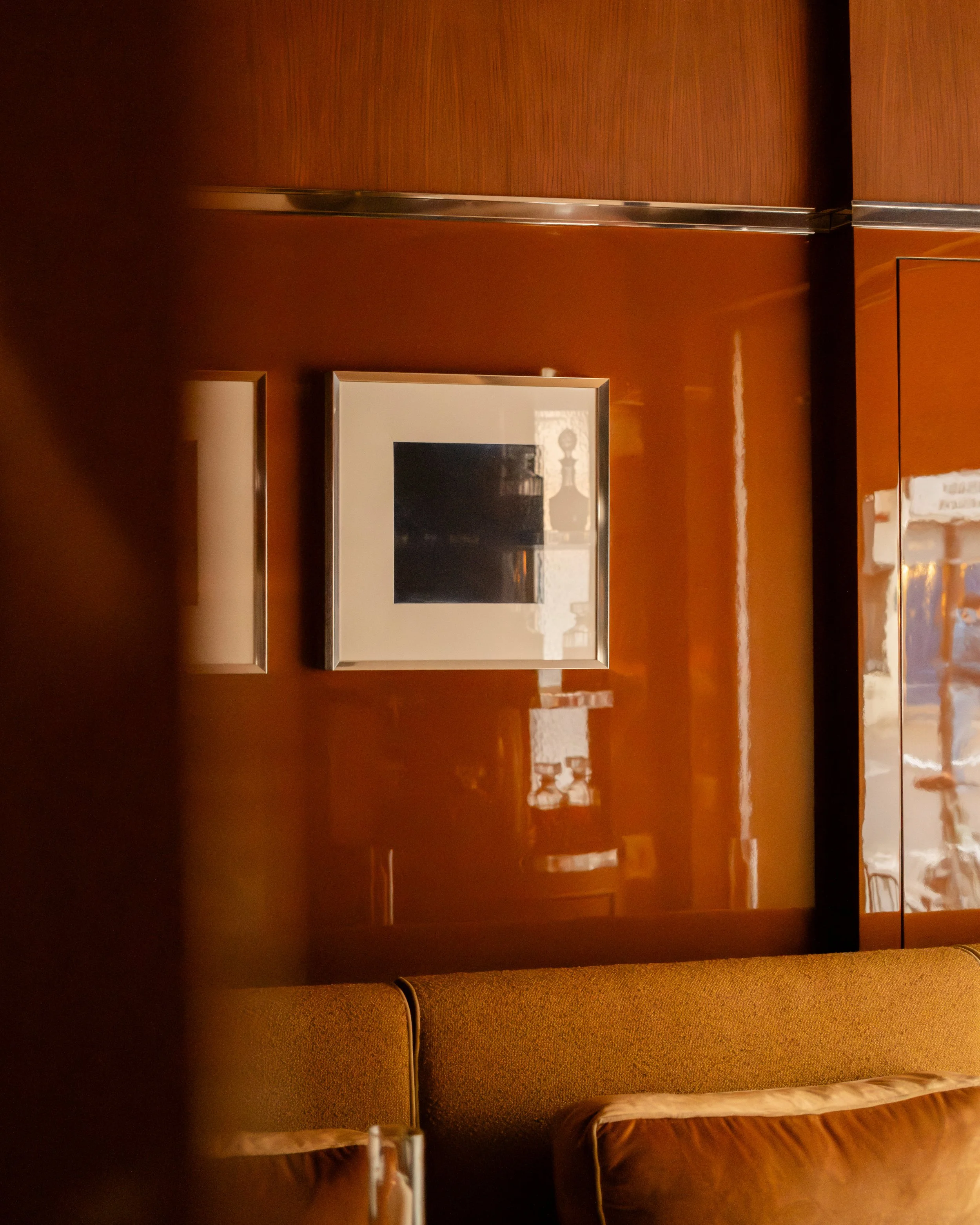 A lounge area with a brown wall, a cushioned bench, and framed artwork on the wall. Lionel Chu - Hotel & Travel Photography