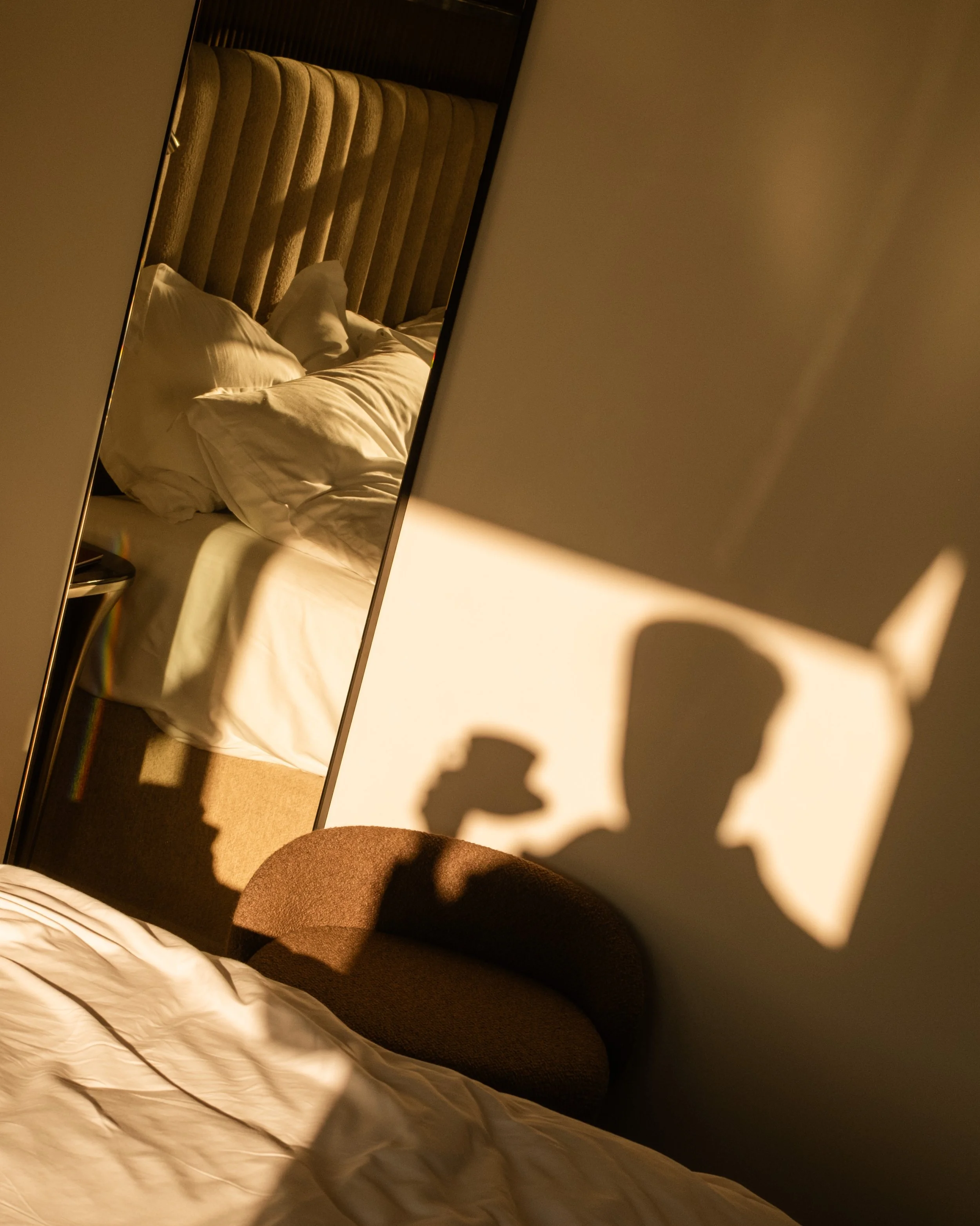 Sunlight casting the shadow of a man holding a coffee cup and a phone on the wall and blanket. Lionel Chu - Hotel & Travel Photographer