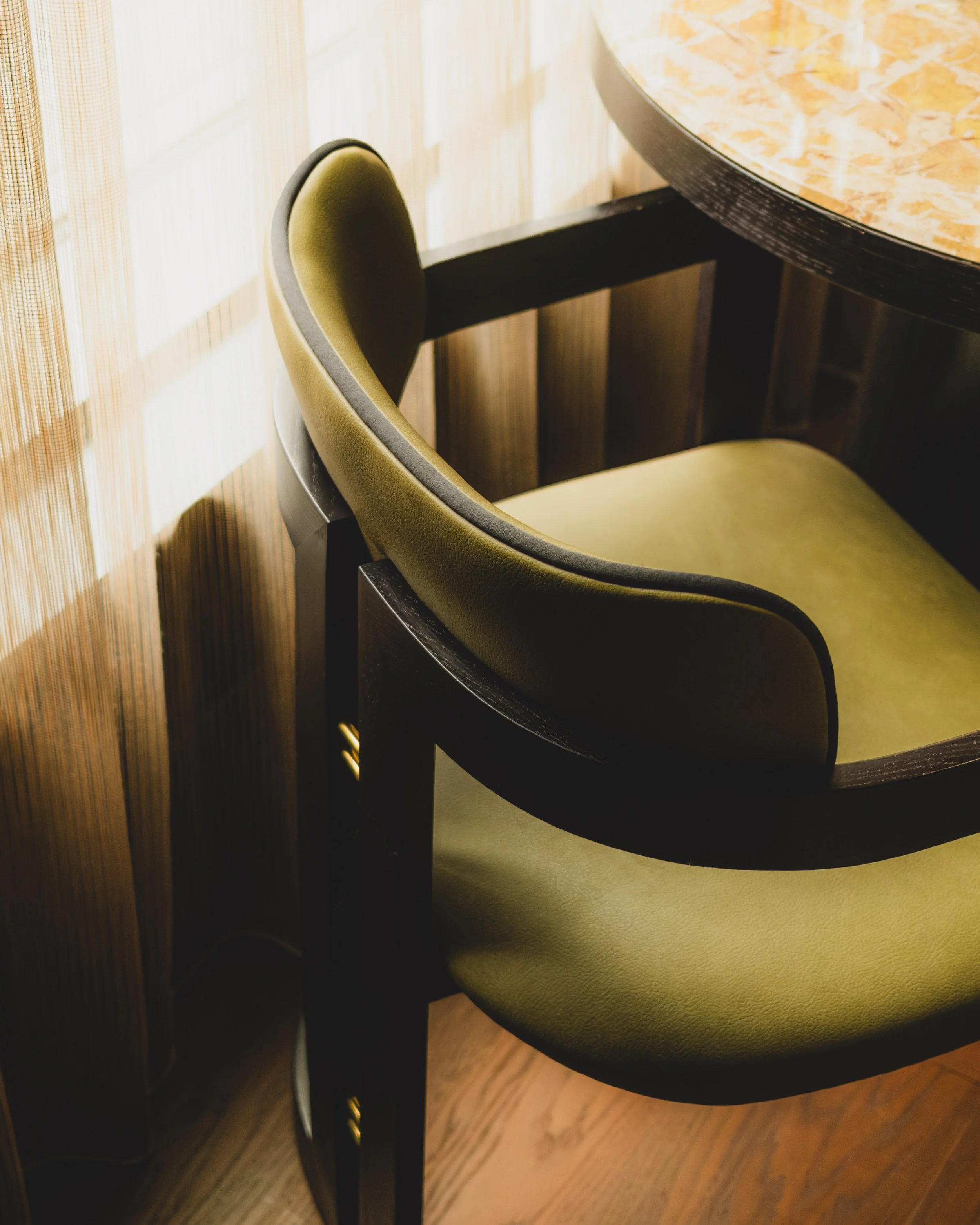 A green upholstered chair with black trim next to a marble-topped wooden table.