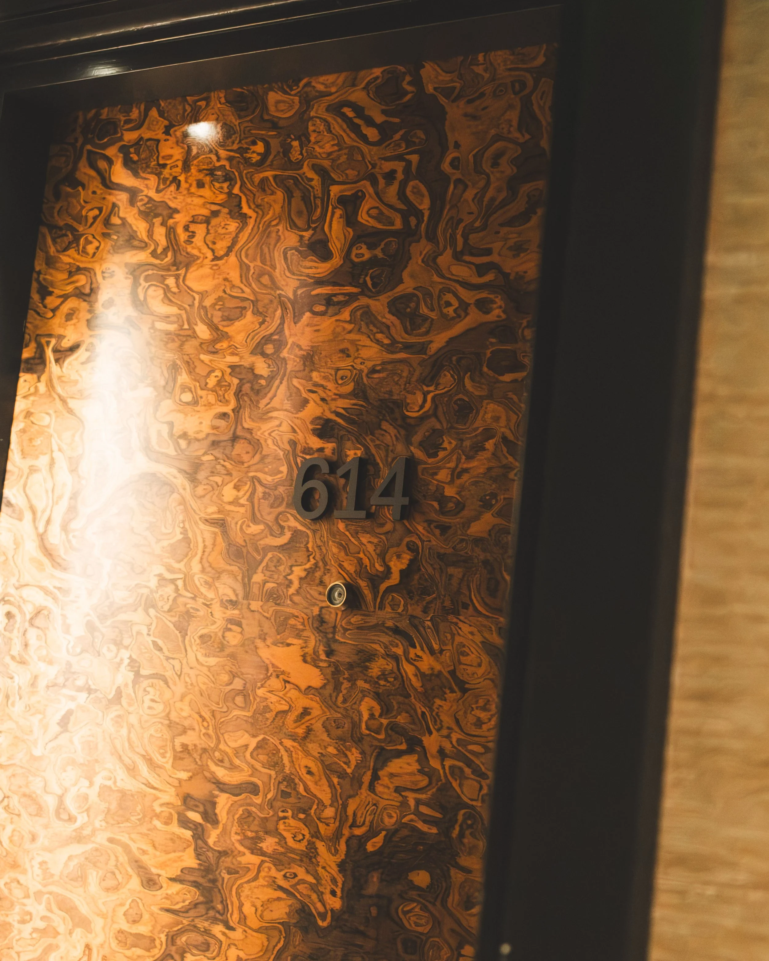 Close-up of an elevator control panel with a textured, marbled wood-like background and black numbers, including 614, and part of the elevator cabin door.