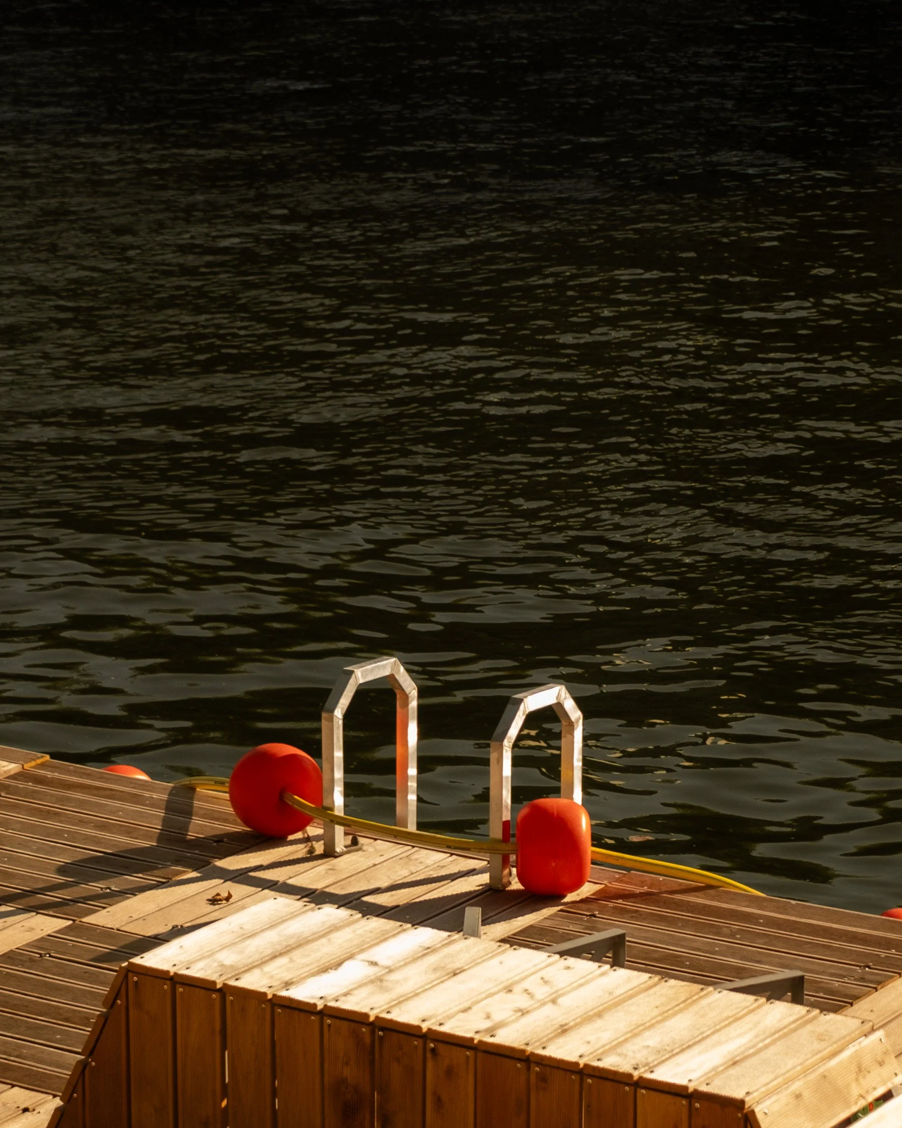 A wooden dock with metal handrails, orange buoys, and a yellow rope against dark water at sunset. Lionel Chu - Hotel & Travel Photographer