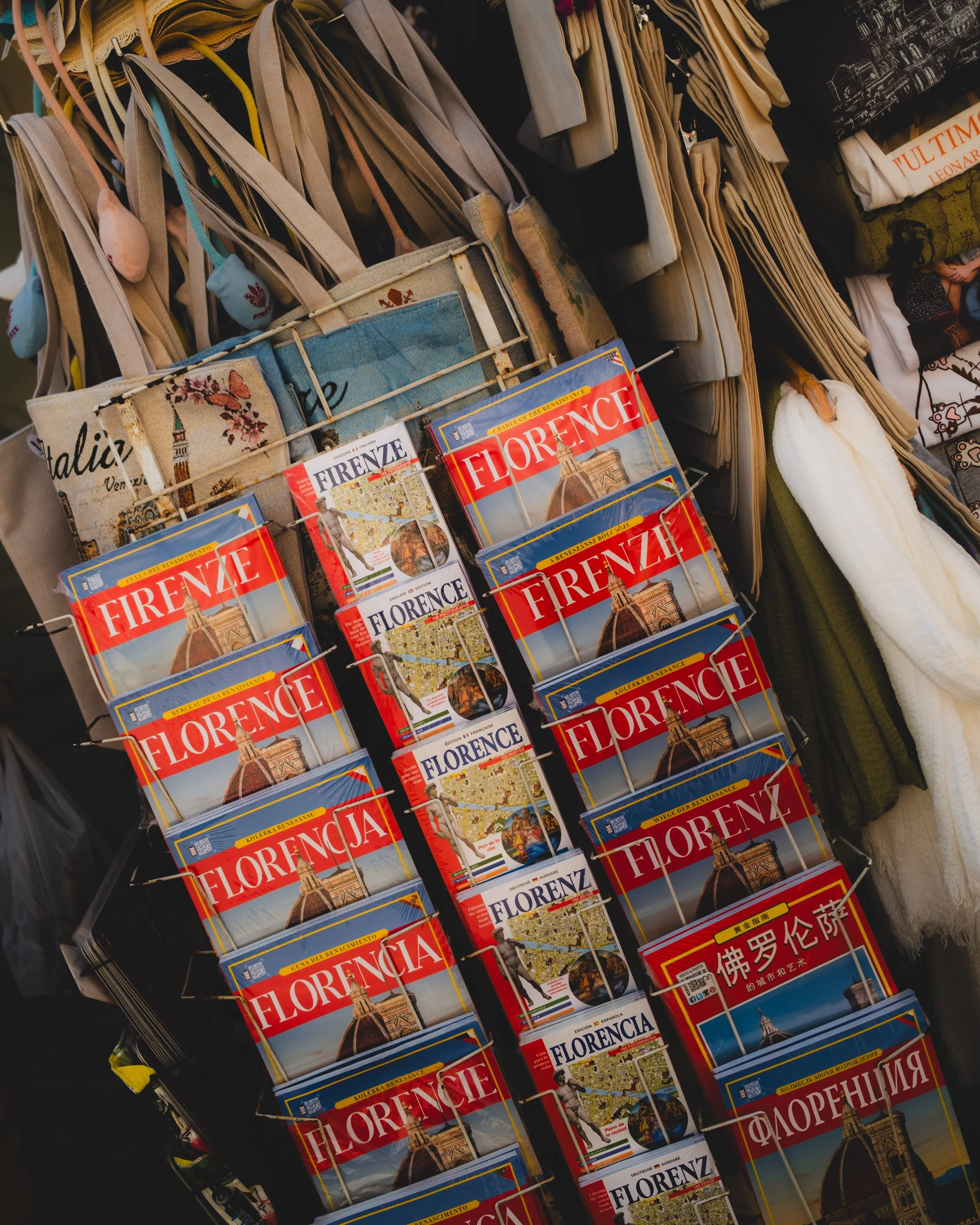 Tourist postcards of Florence, Italy, featuring iconic landmarks like the Florence Cathedral, displayed on a rack among travel souvenirs. Lionel Chu - Hotel & Travel Photographer
