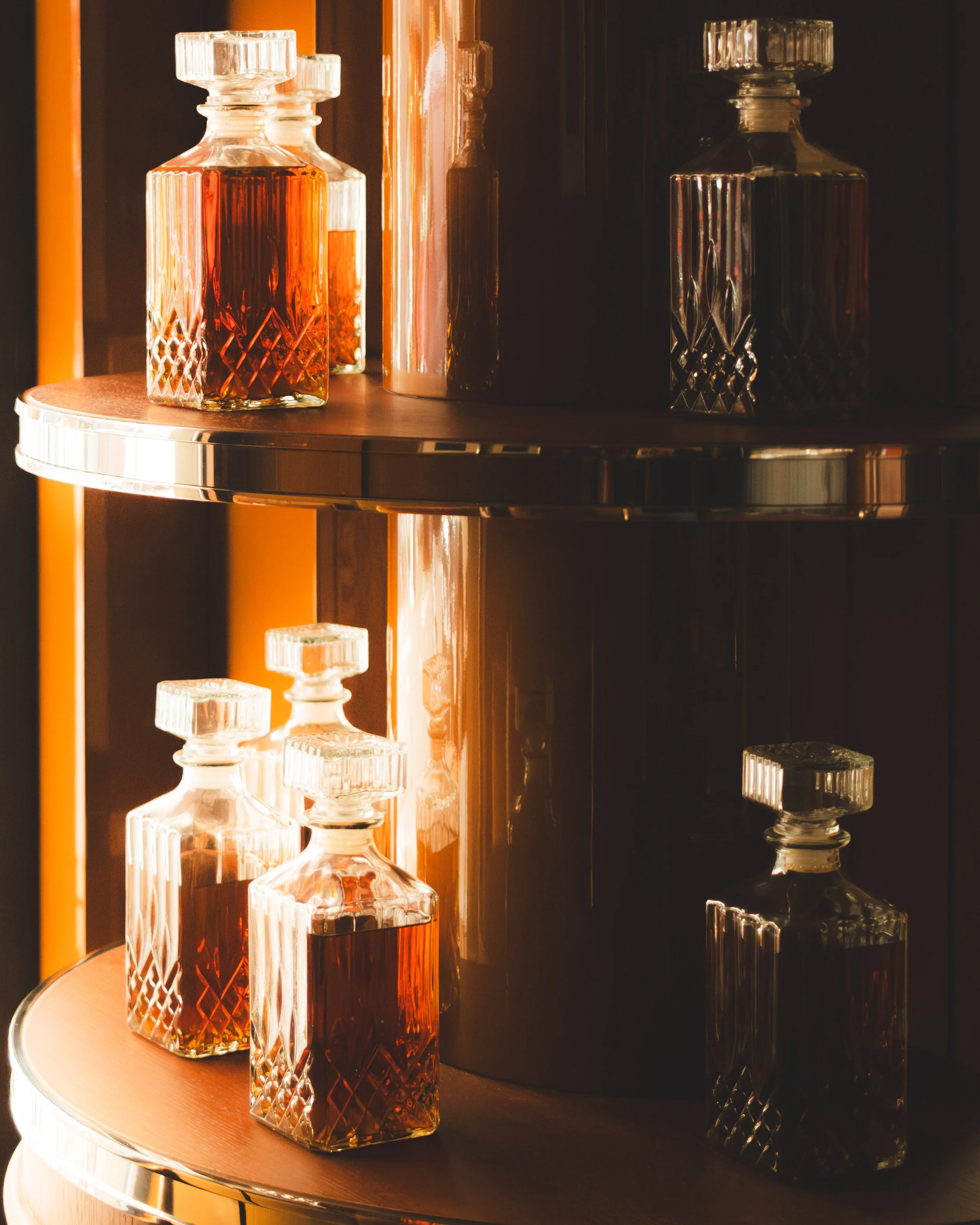 Glass perfume bottles with geometric patterns on a wooden and metallic surface, reflected in a mirror.