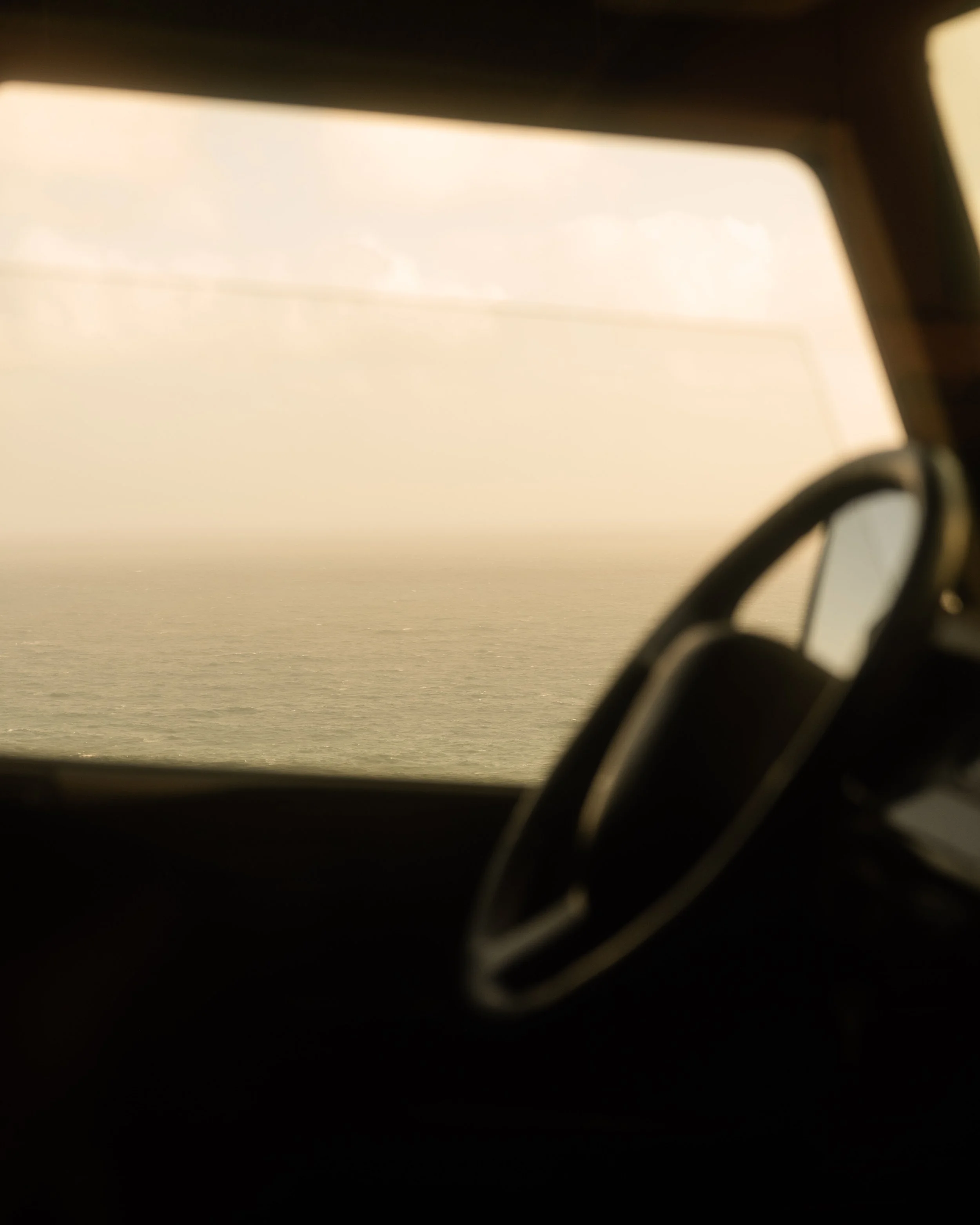 A close-up view of a side mirror of a vehicle reflecting the sky and clouds during sunset or sunrise, with a partial view of the car's window and interior.