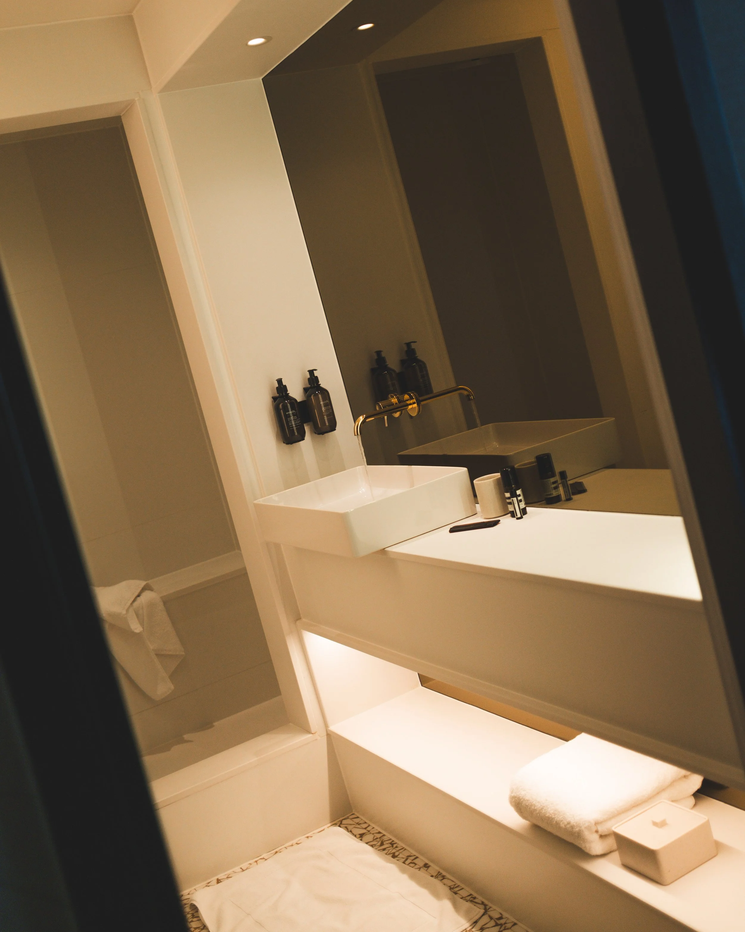 Bathroom or vanity area with open shelves, a sink, a mirror, toweling, and toiletries, illuminated by warm lighting.