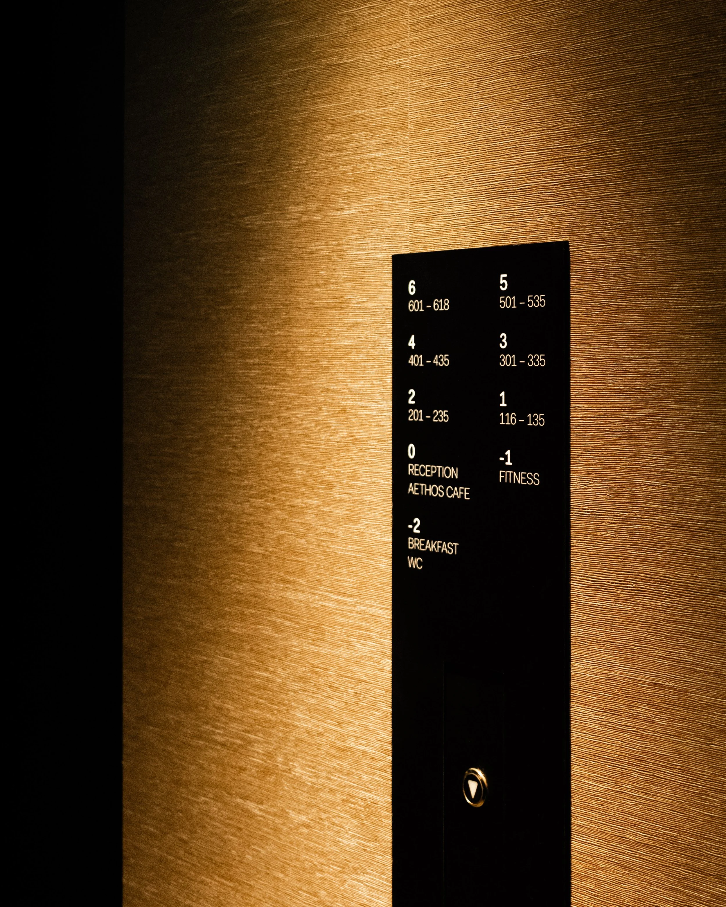 Elevator directory sign displaying floor numbers and room ranges in a hotel or building, with a textured brown wall background. Lionel Chu - Hotel & Travel Photographer