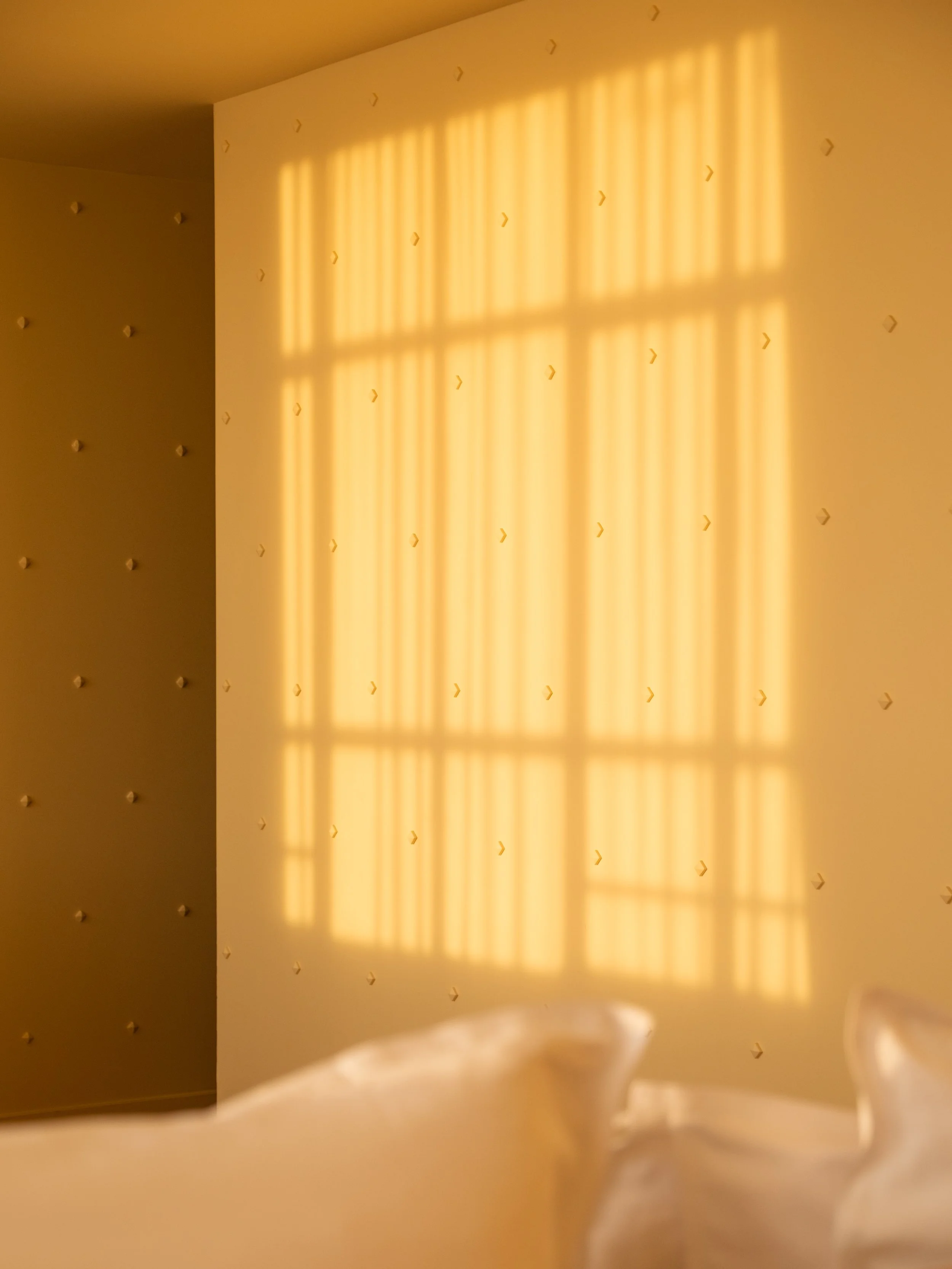 Sunlight casting shadows of window blinds on a beige wall. Lionel Chu - Hotel & Travel Photography