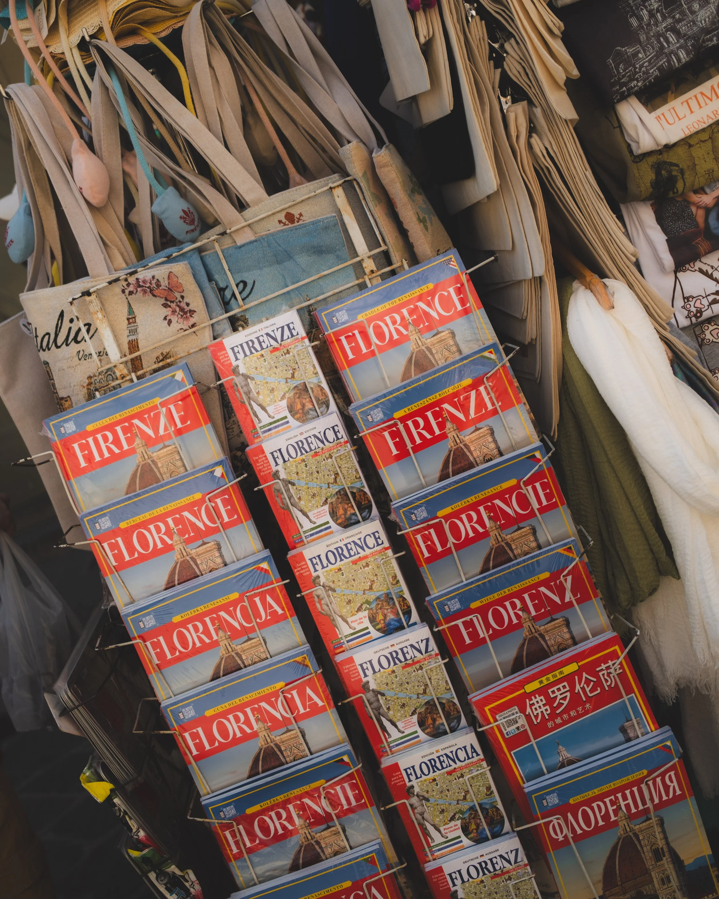 Tourist postcards of Florence, Italy, featuring iconic landmarks like the Florence Cathedral, displayed on a rack among travel souvenirs. Lionel Chu - Hotel & Travel Photographer