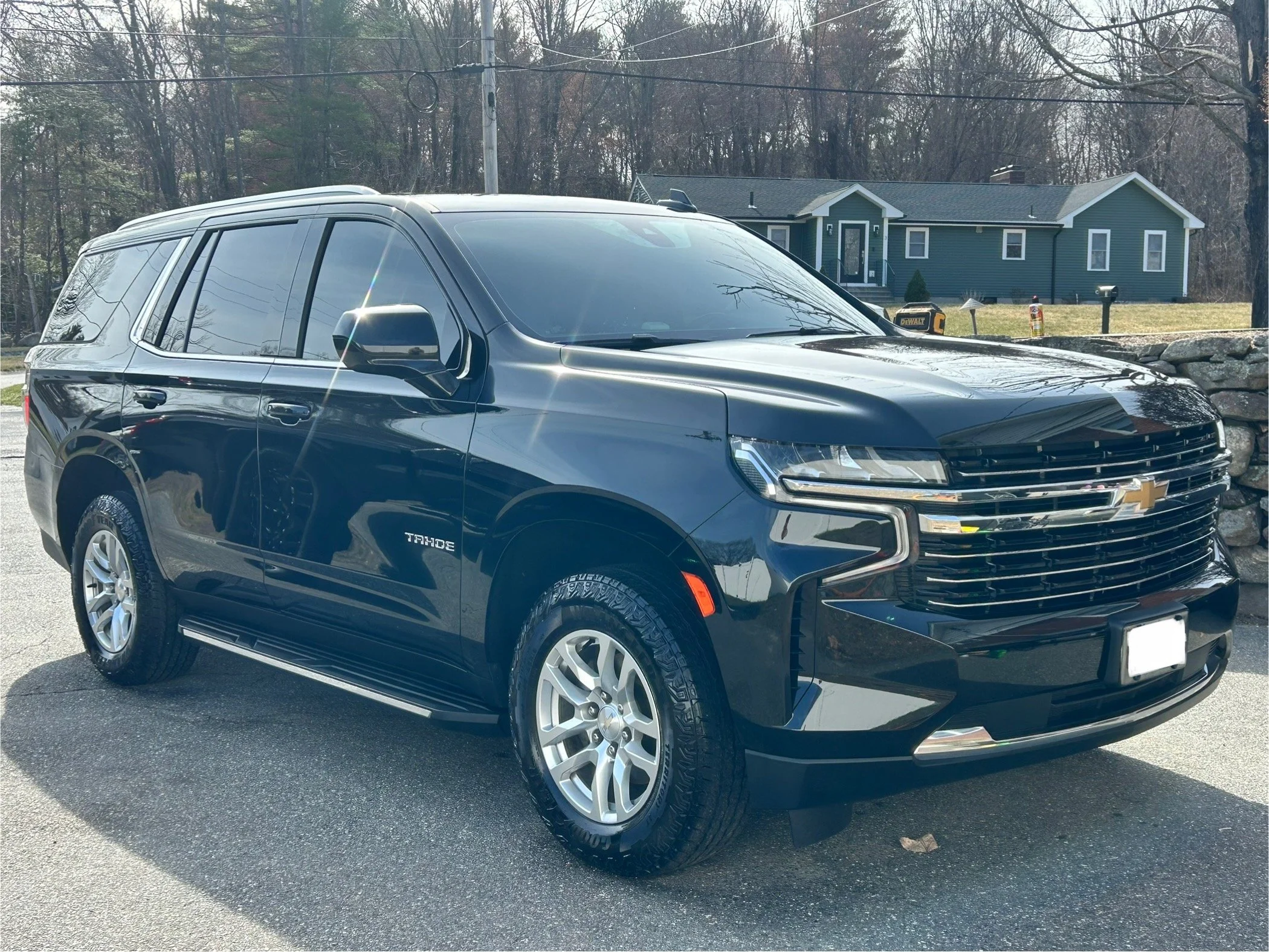 Black Chevrolet Tahoe parked on a residential street with a house and trees in the background.